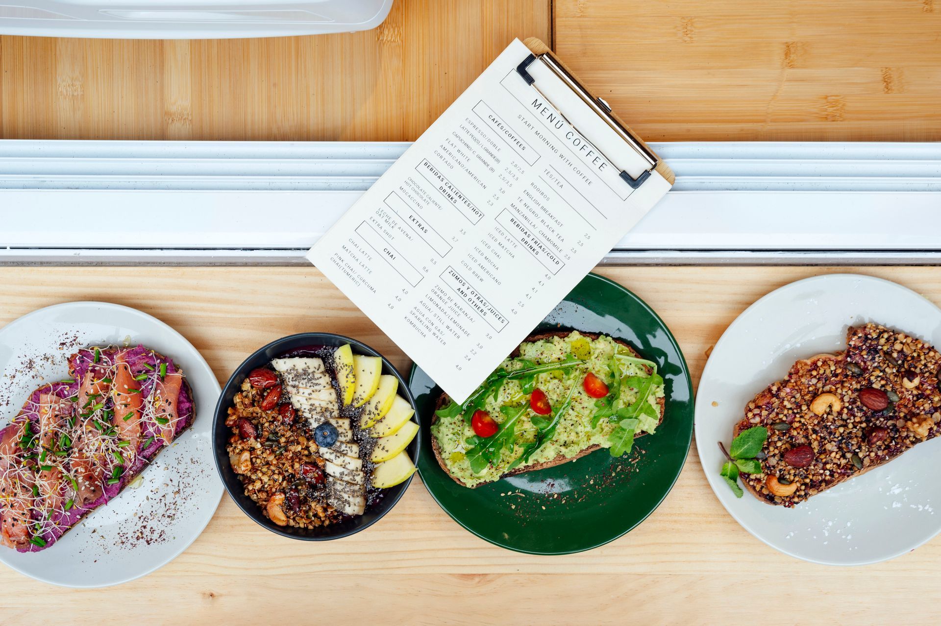 Flat lay of colorful vegan dishes with menu clipboard on wooden table at trendy vegan restaurant.