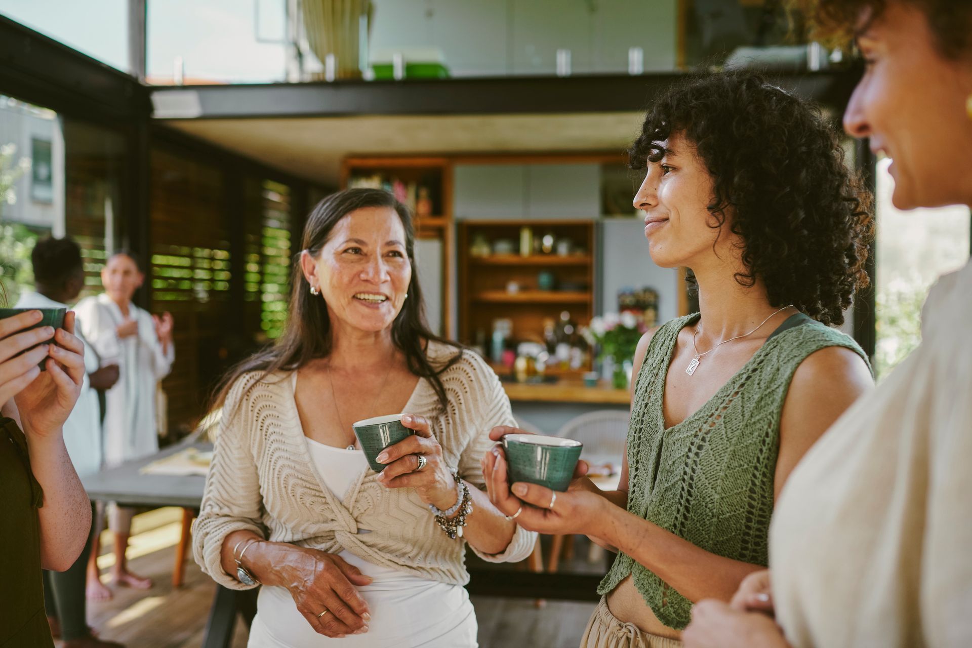 Diverse group of smiling female friends talking and drinking cups of herbal hot tea in a tea house.