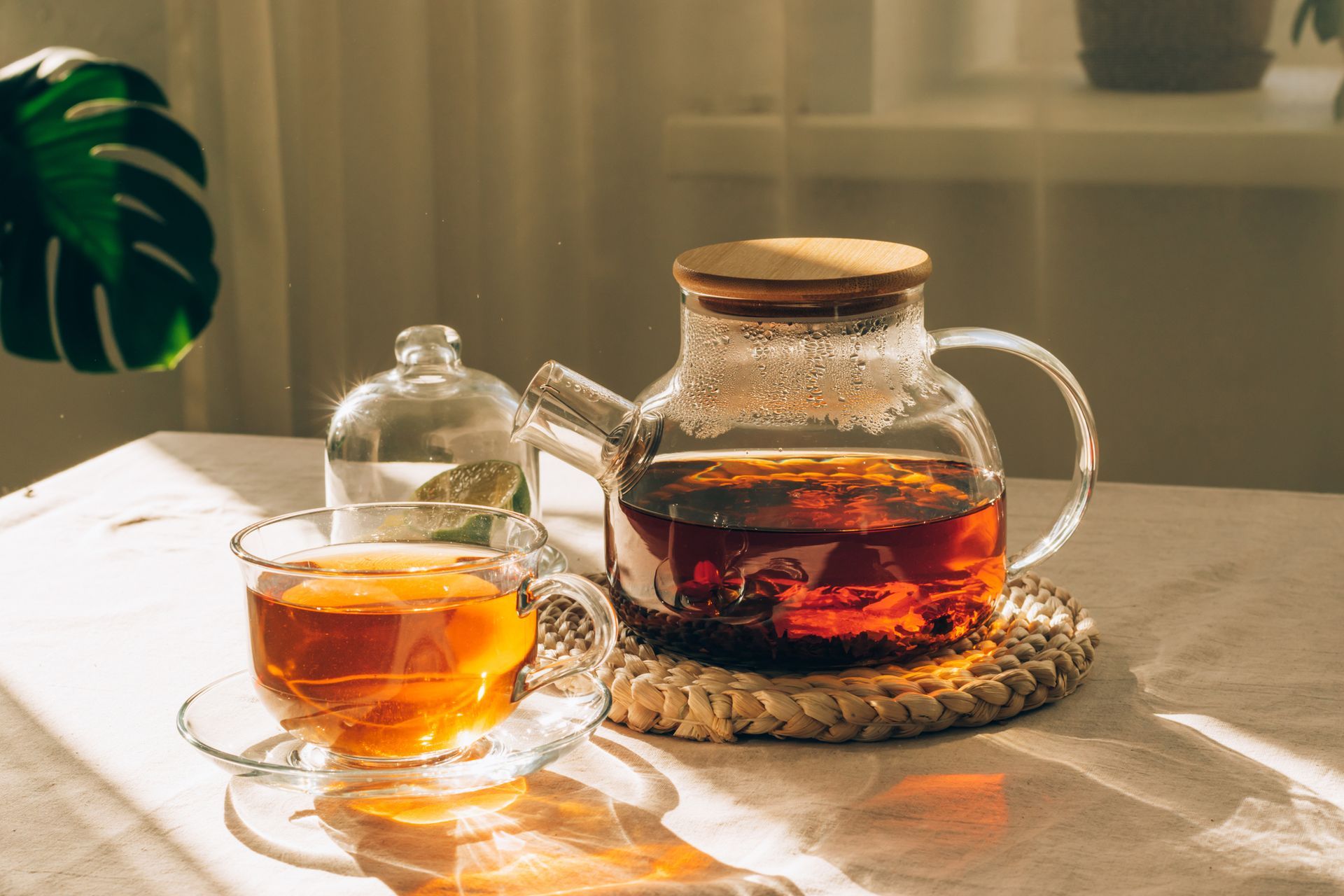 Hot tea or flower tea in a glass tea kettle surrounded by glass tea cups on a round wooden tray.