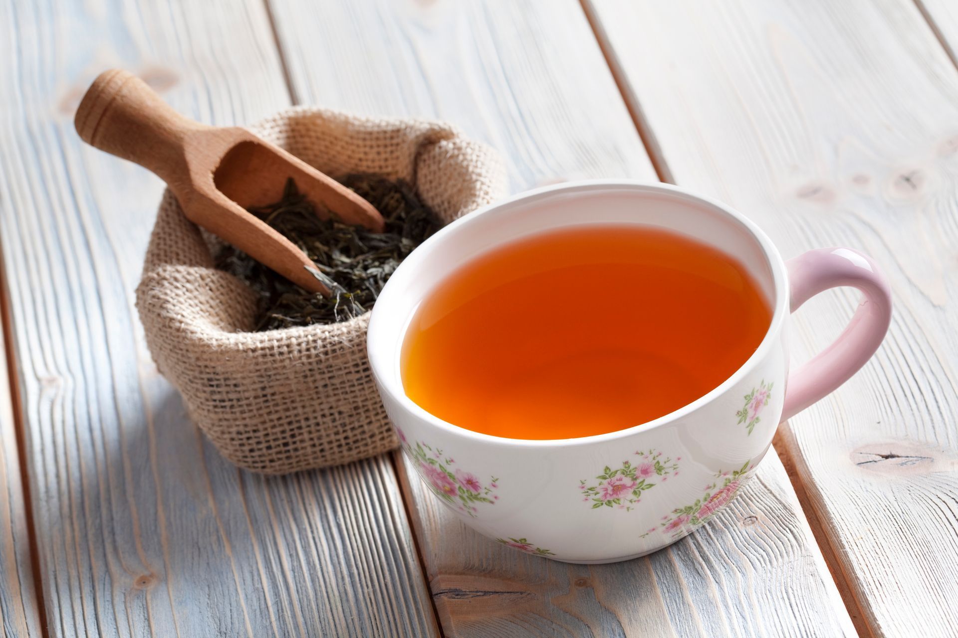 Cup of tea next to a burlap sack filled with loose tea leaves; wooden scoop rests in the sack.