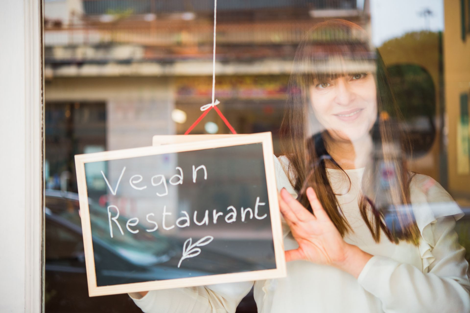 Vegan restaurant owner working with “vegan” sign visible behind glass door. Vegan restaurant owner working with “vegan” sign visible behind glass door.