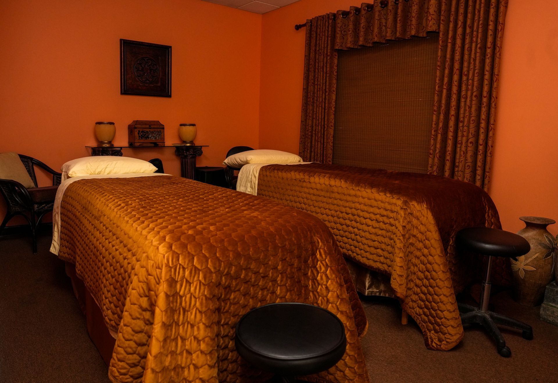 Two twin beds in a warmly lit hotel room with orange walls and brown curtains.