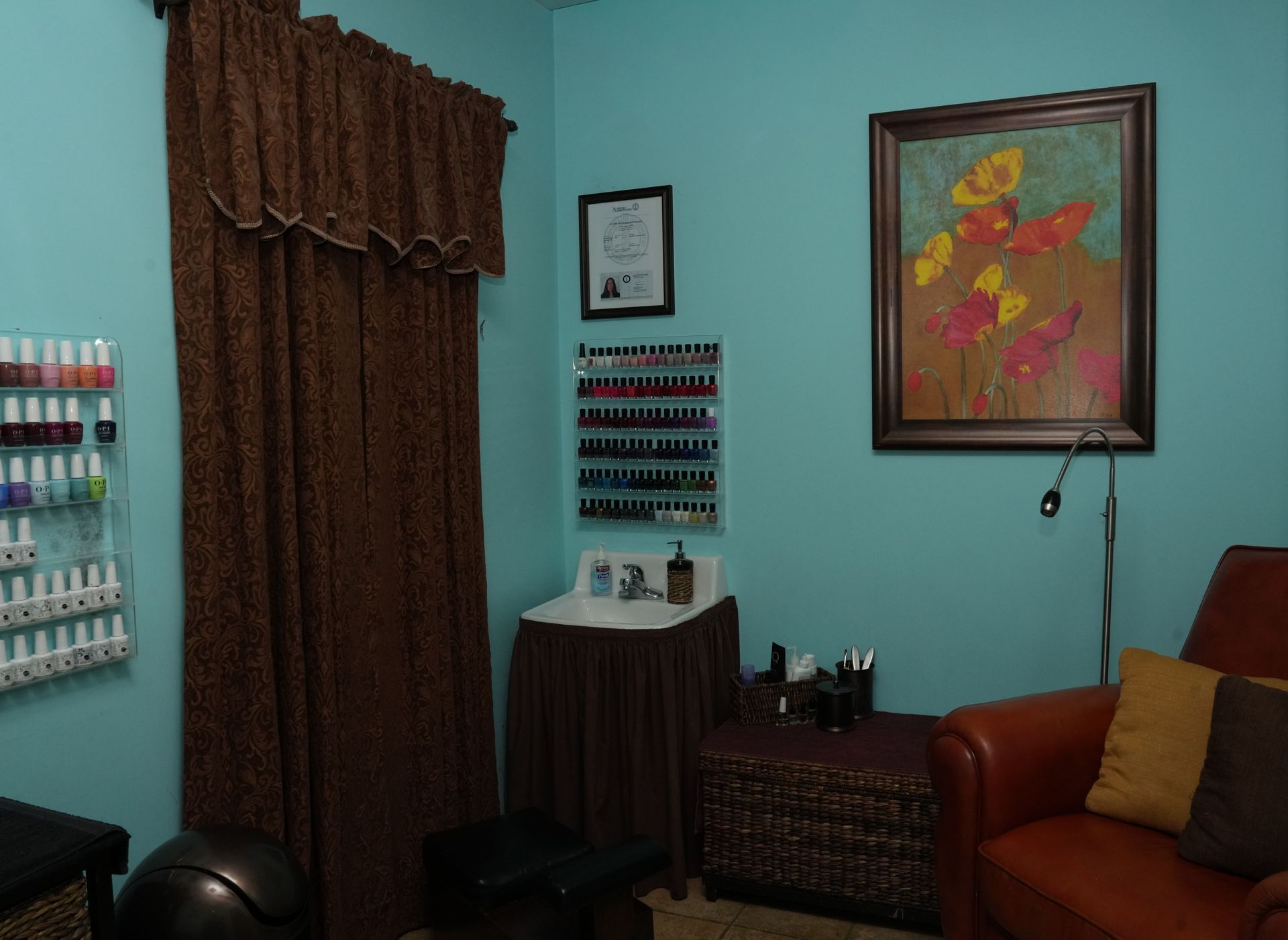 Turquoise room with nail polish display, framed art, brown curtains, and a sofa in the corner