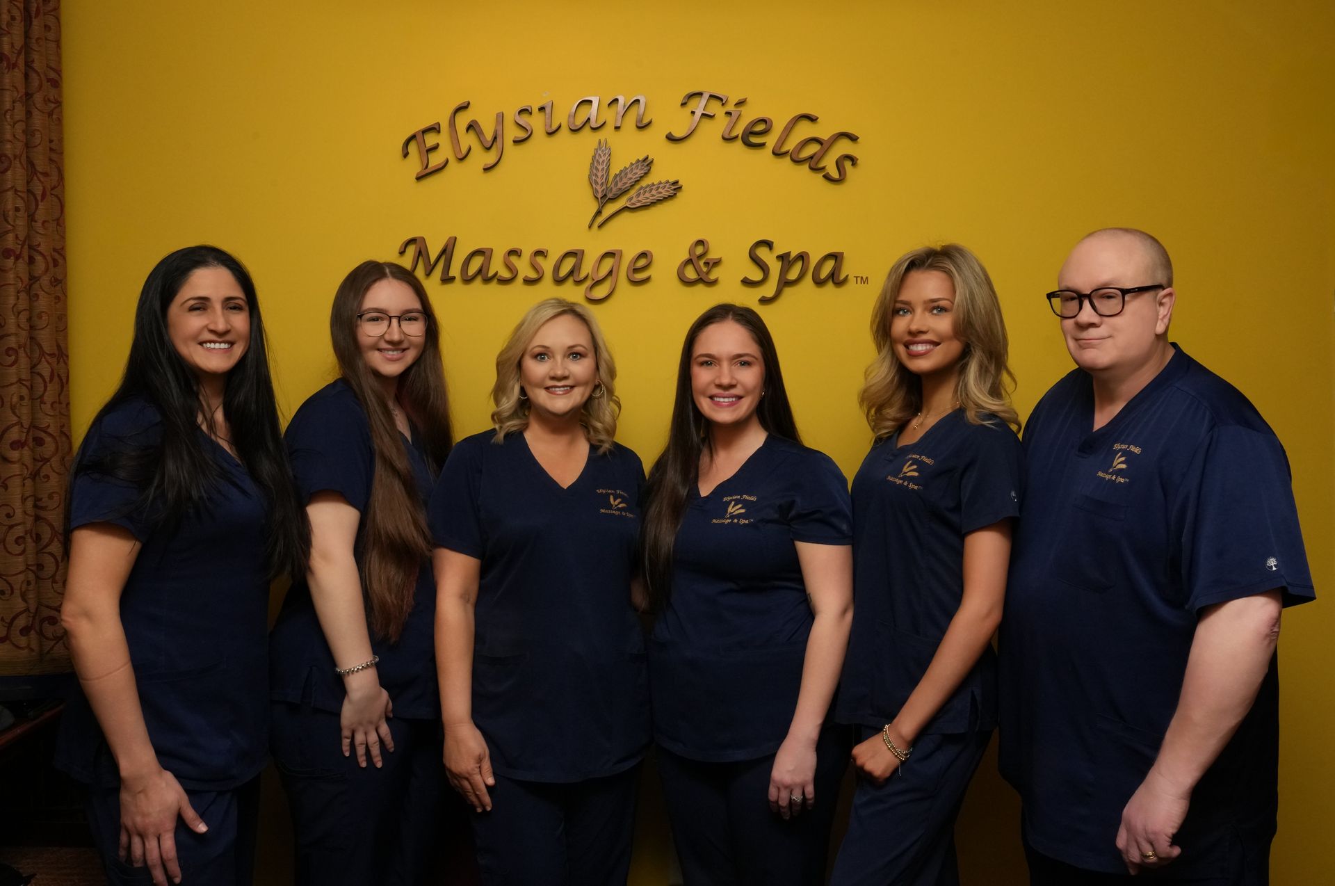 Six people in navy uniforms standing in front of the Elysian Vela Massage & Spa sign.