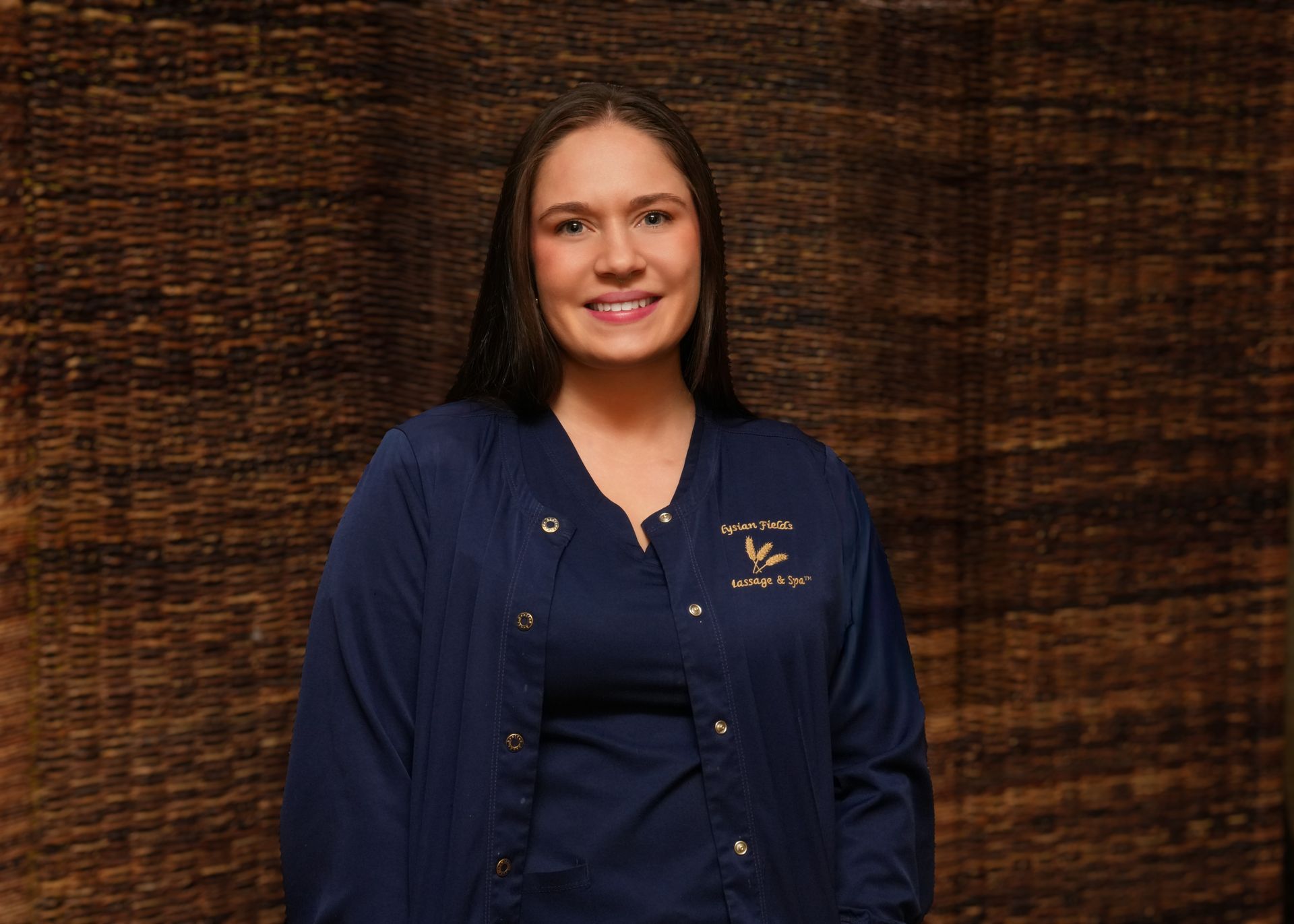 Woman standing against a dark textured wall, wearing a navy jacket and smiling.