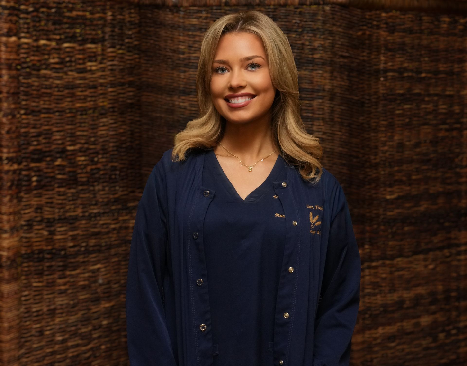 Smiling woman in a navy blouse and cardigan standing before a dark woven backdrop