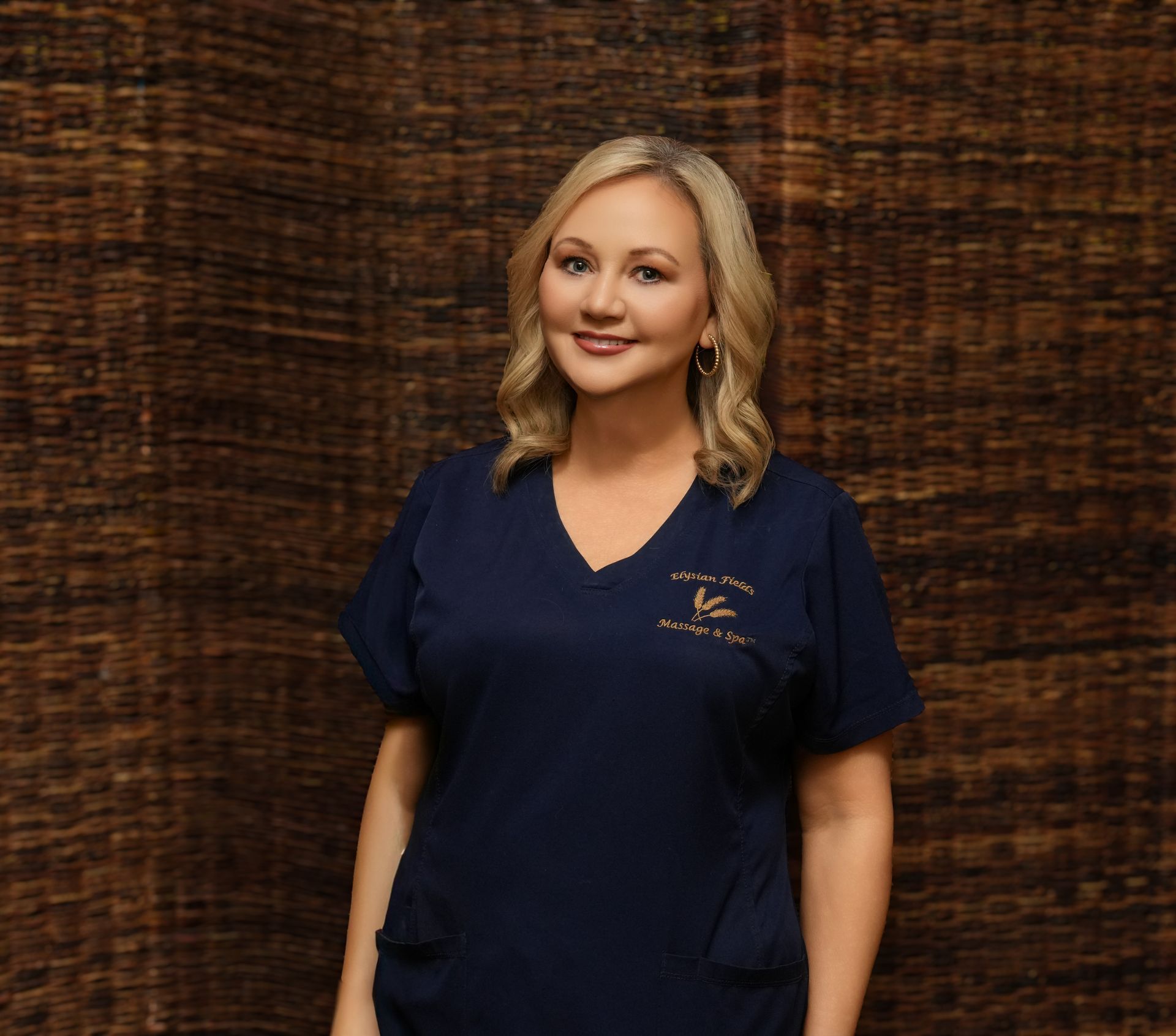 Woman in navy scrubs smiling against a textured brown backdrop