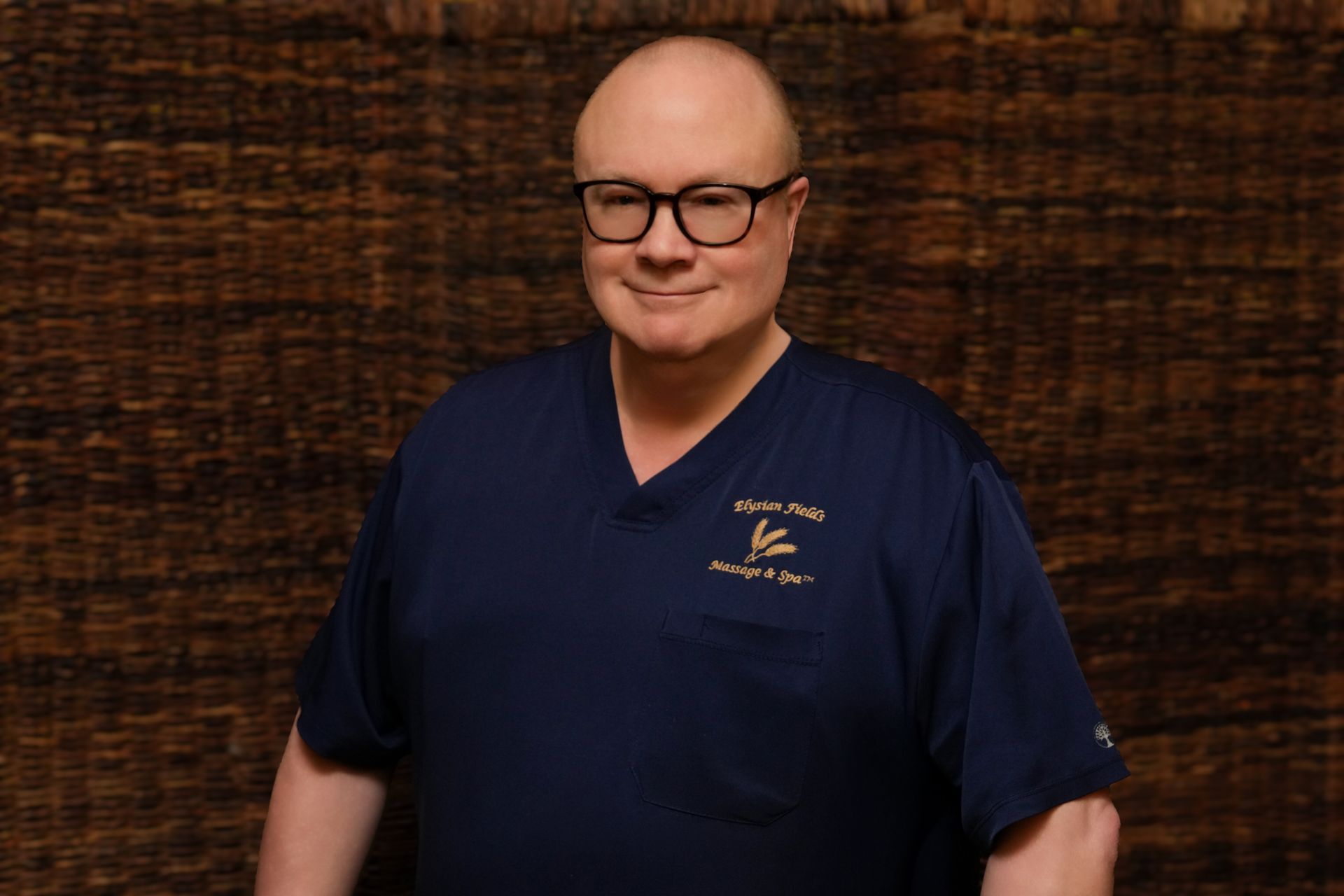 Smiling man in glasses wearing a navy shirt against a dark wood wall