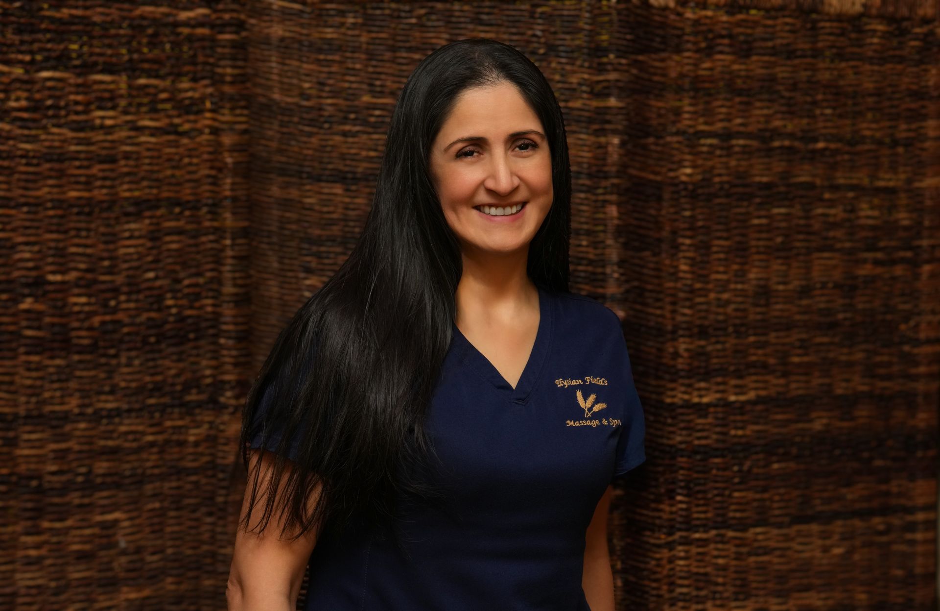 Smiling woman in a navy polo shirt standing before a woven brown backdrop