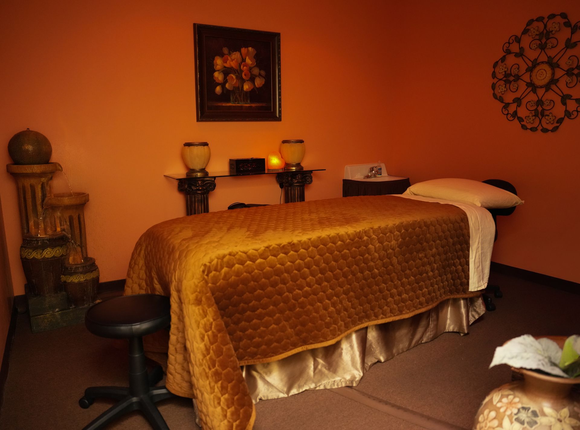 Spa treatment room with a massage table, orange walls, candles, and decorative accents.