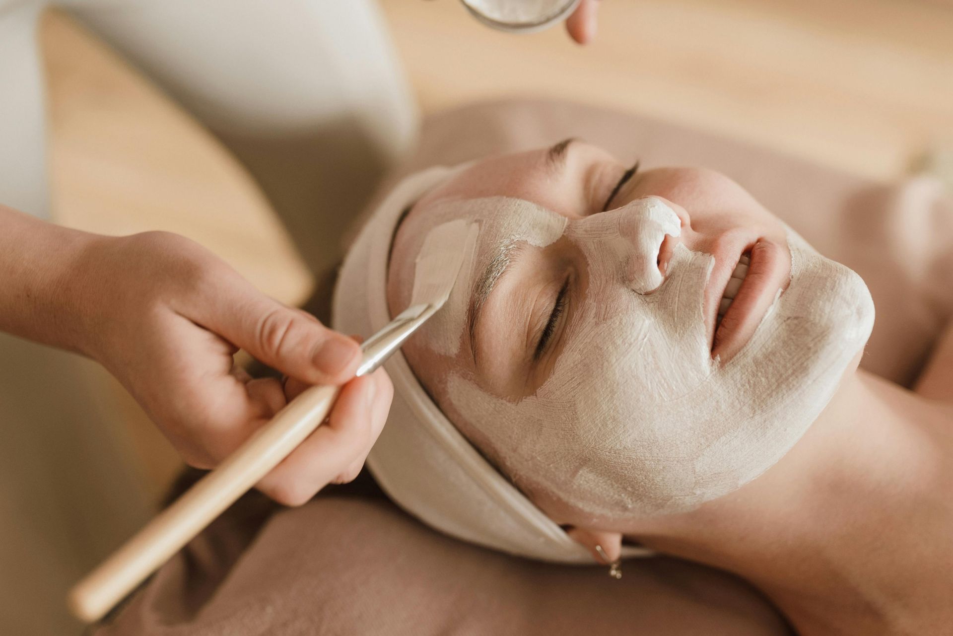 Facial mask being applied with a brush at a spa, with a person relaxing under a towel