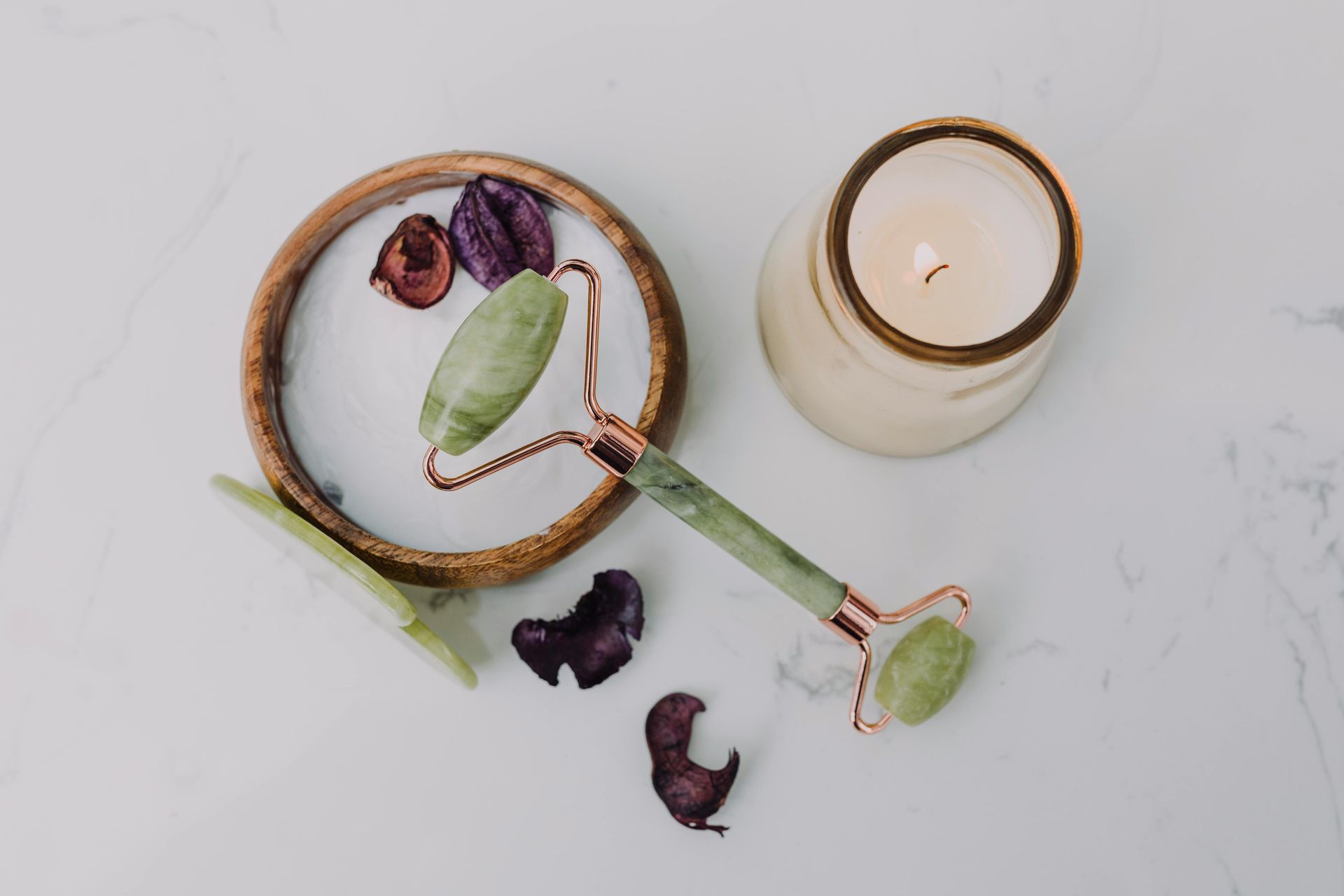Tea strainer with dried petals beside a lit candle on a white surface