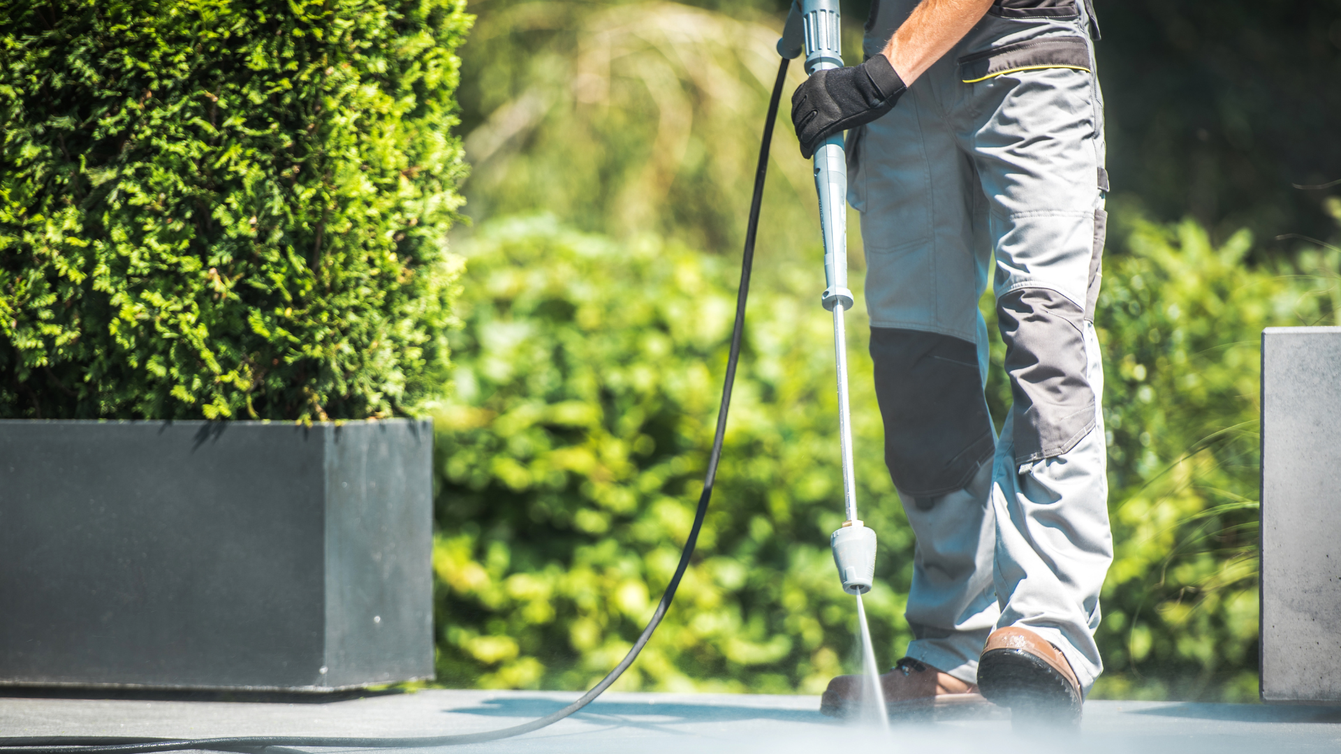 A man is using a high pressure washer to clean a sidewalk.