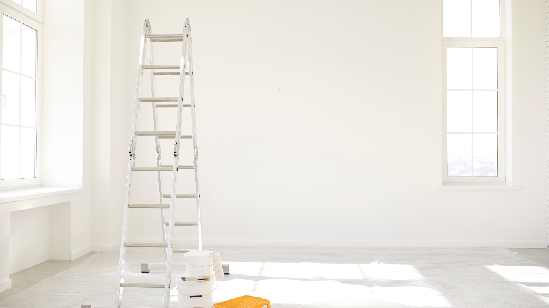 An empty room with a ladder and paint buckets in it.