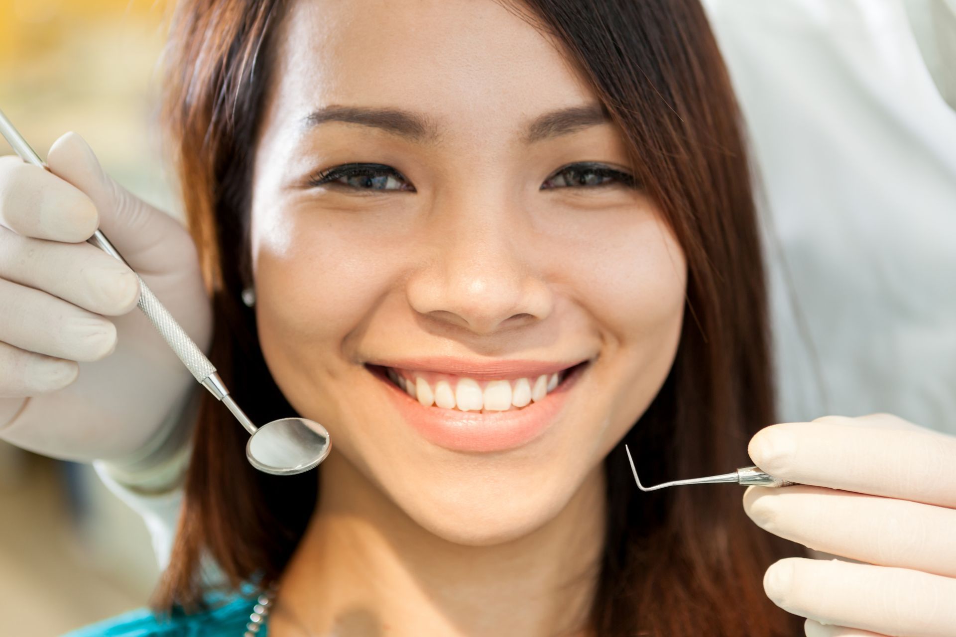 A close-up of a woman smiling and sitting at the dentist. The dentist holds dental tools