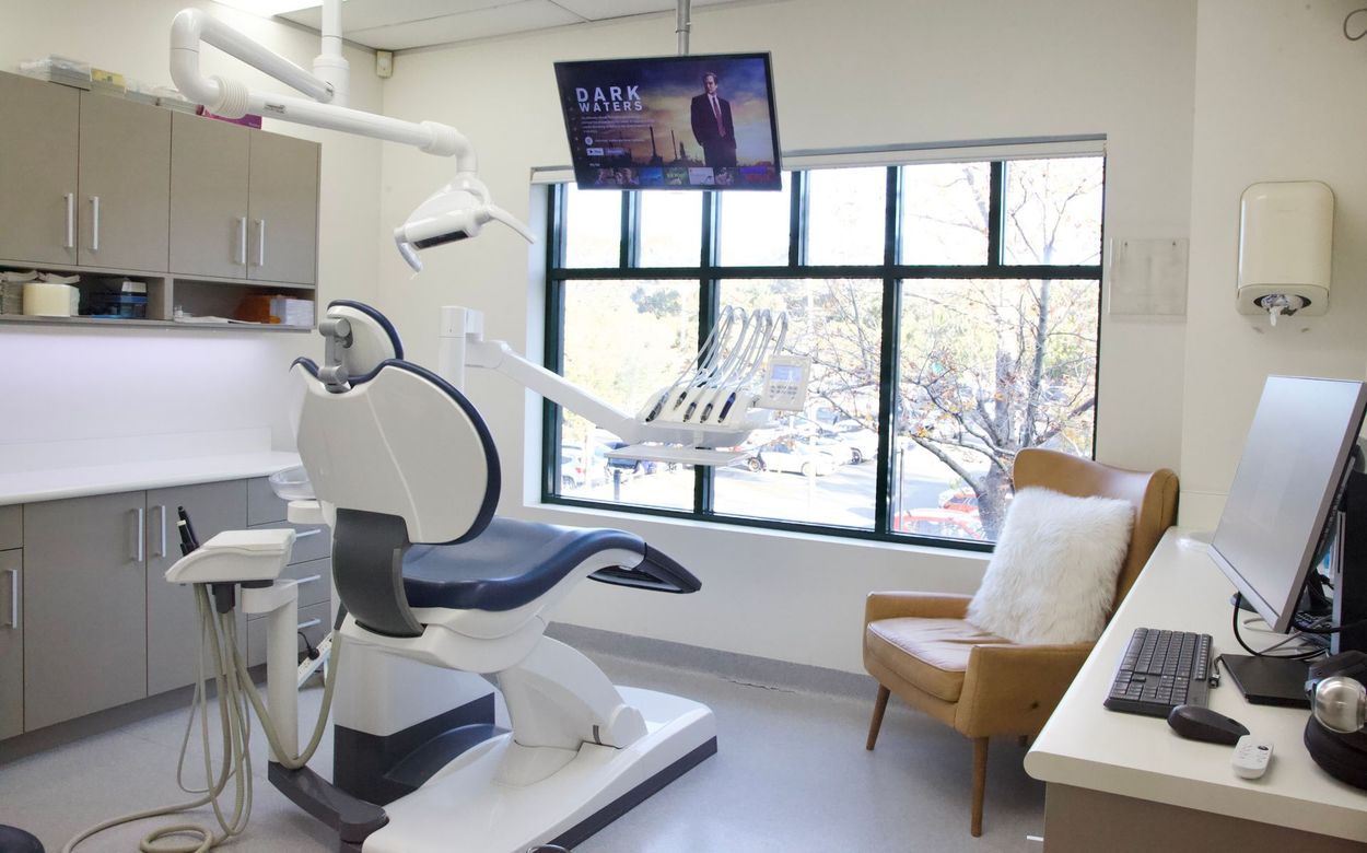 A dental office with a dental chair , chair , desk and computer.