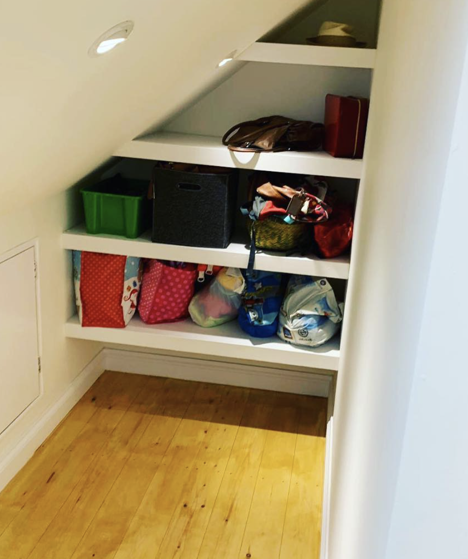 A closet under a staircase filled with boxes and bags