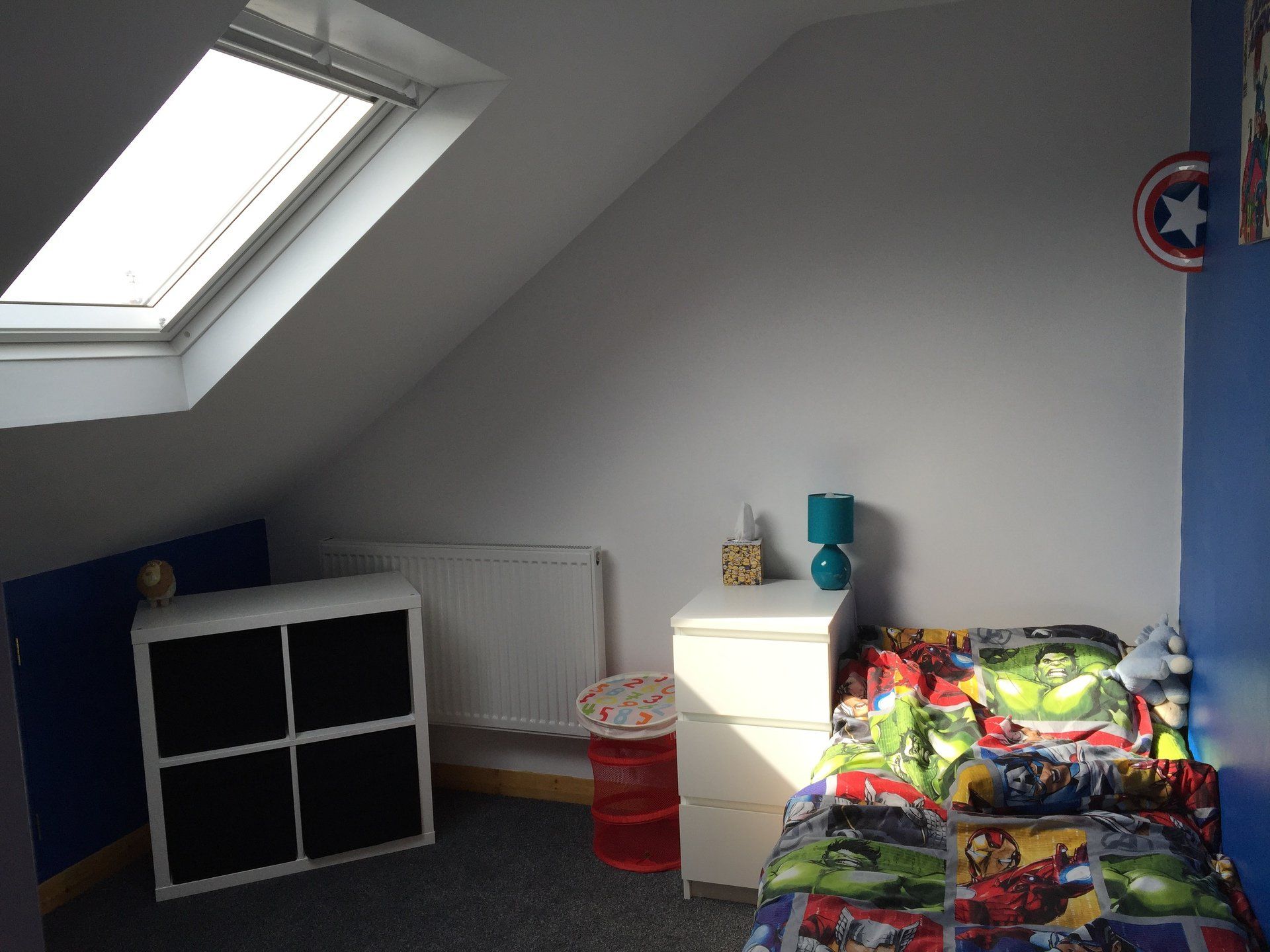 A bedroom with a bed , nightstand , and a skylight.