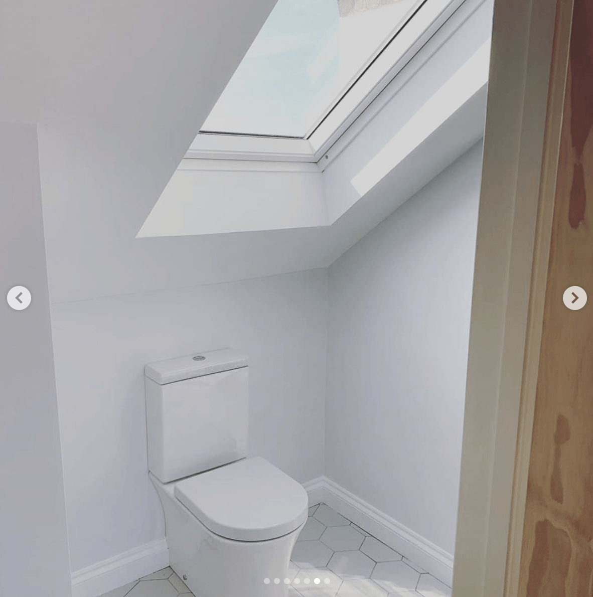 A toilet in a bathroom with a skylight above it