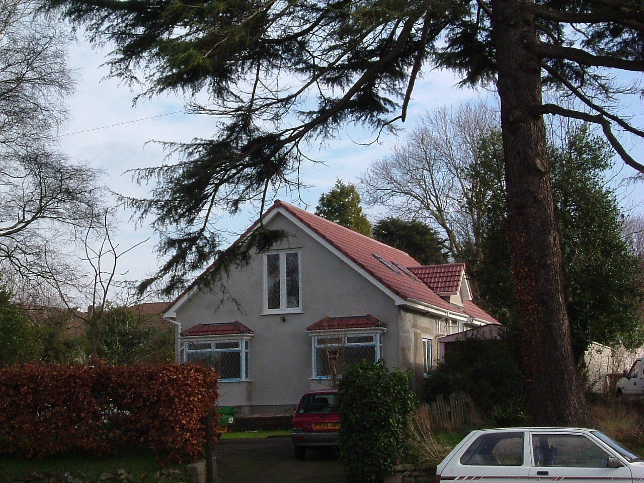 A white car is parked in front of a house with a red roof