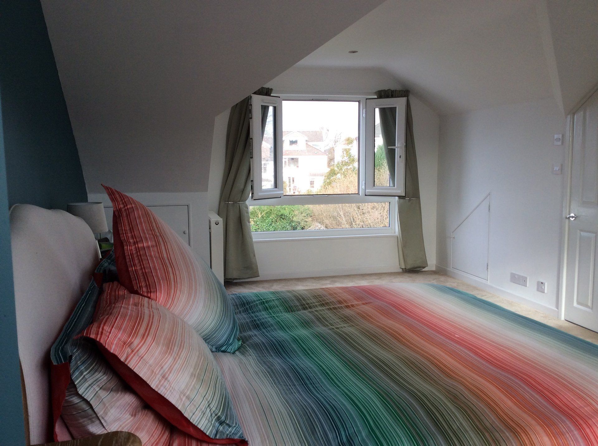 A bedroom with a rainbow colored bed and a window.