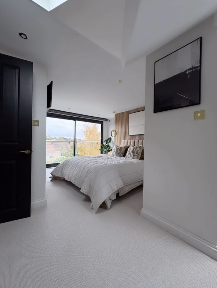 A bedroom with a large bed and a black door of a new loft conversion.