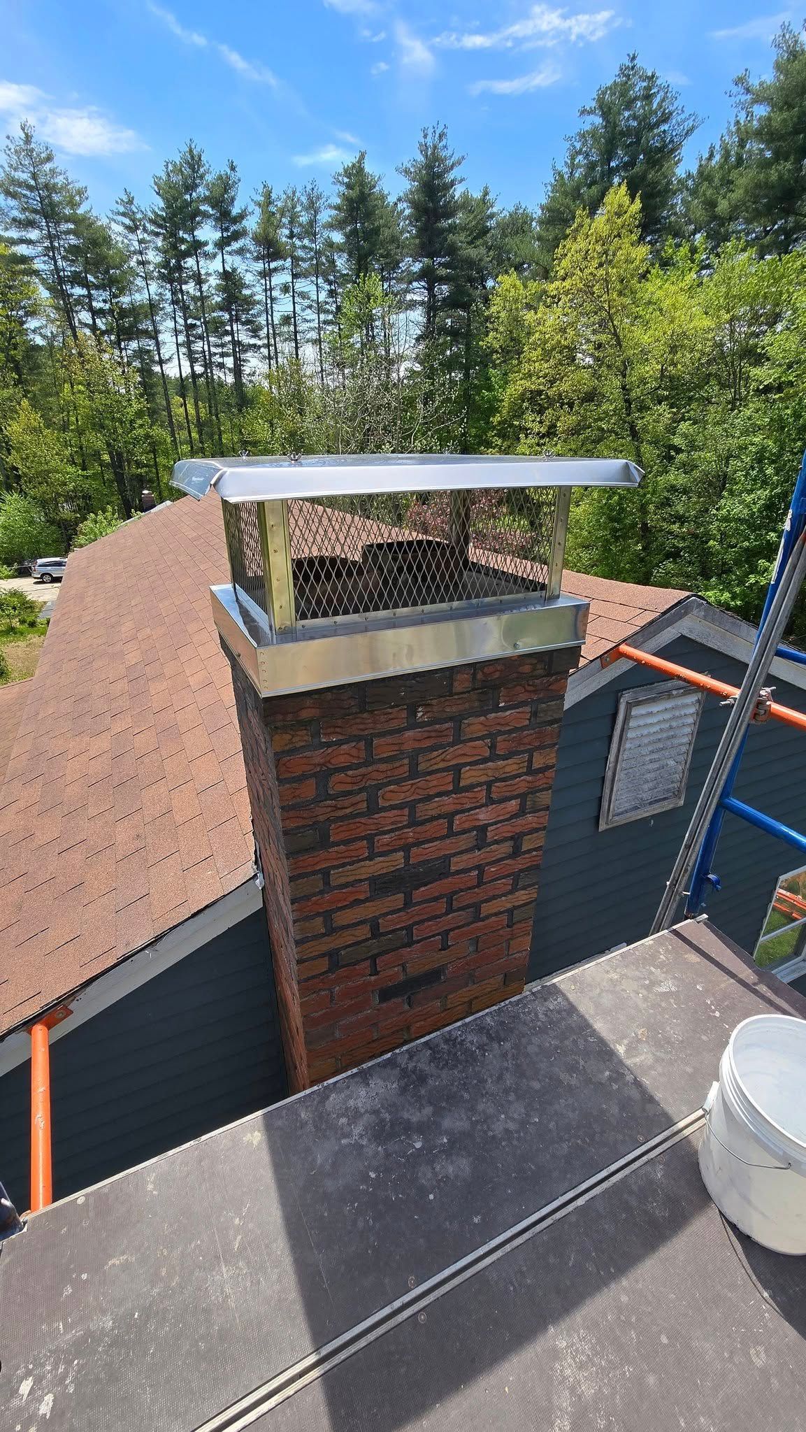 A brick chimney is sitting on top of a roof next to a scaffolding.