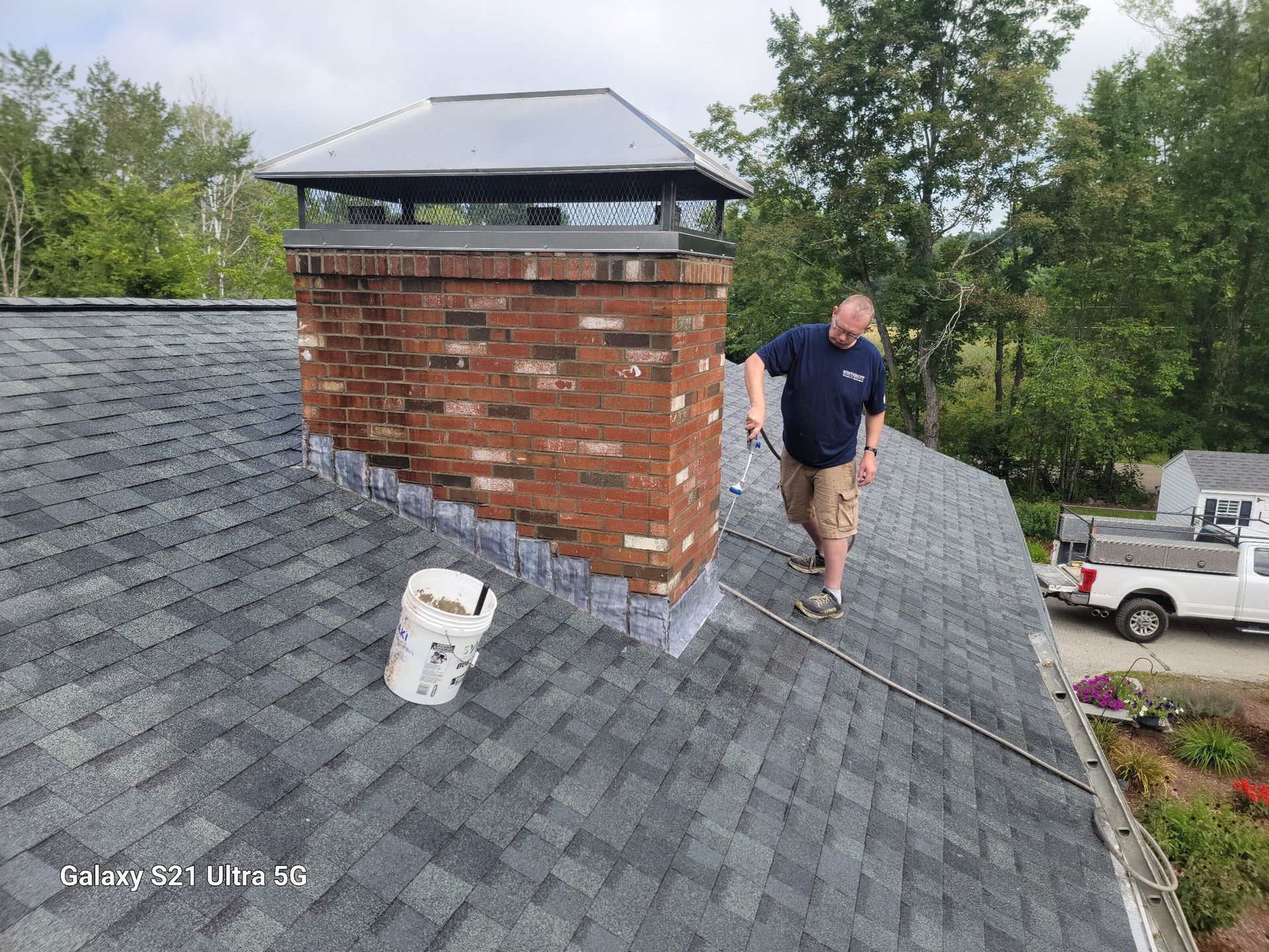 A man is standing on top of a roof next to a chimney.