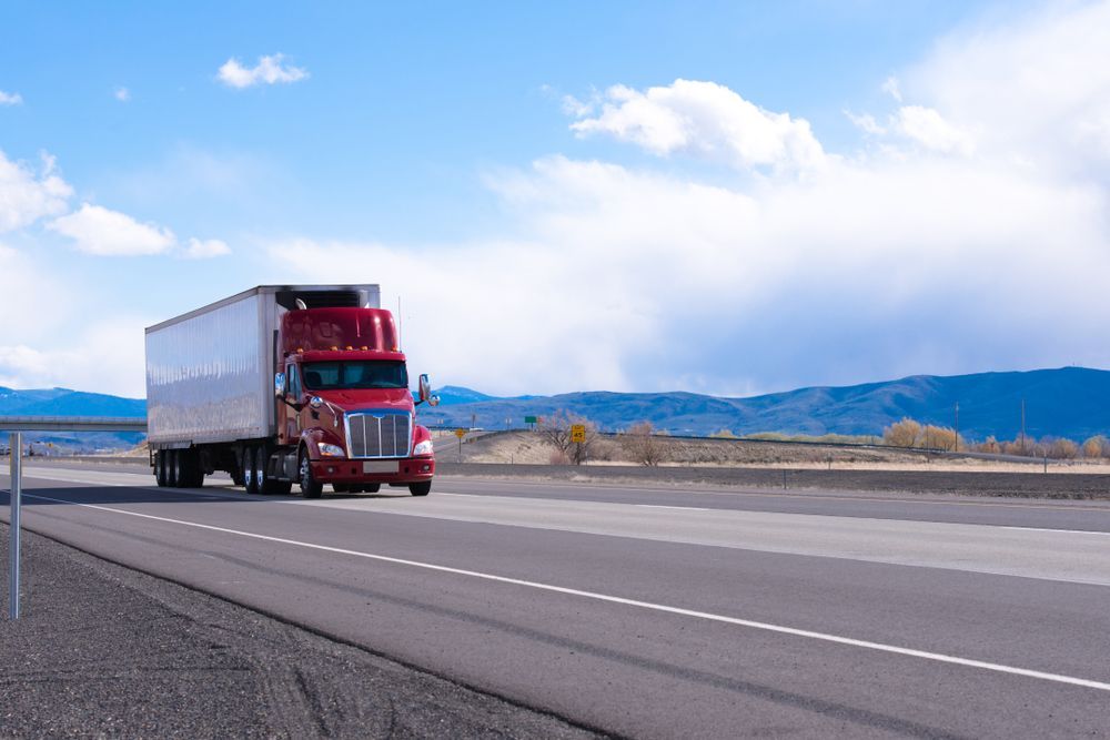 A Red Semi Truck Is Driving Down A Highway With Mountains — R2B Heavy Vehicle Driving School In Paget, QLD