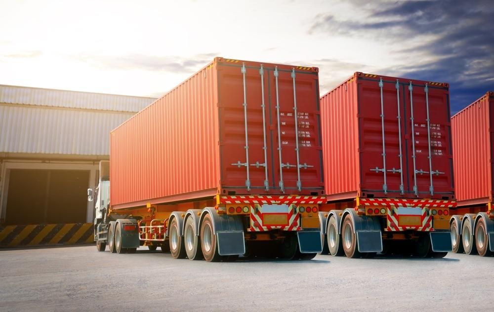 A Row Of Red Shipping Containers Are Parked In Front Of A Warehouse — R2B Heavy Vehicle Driving School In Mackay, QLD