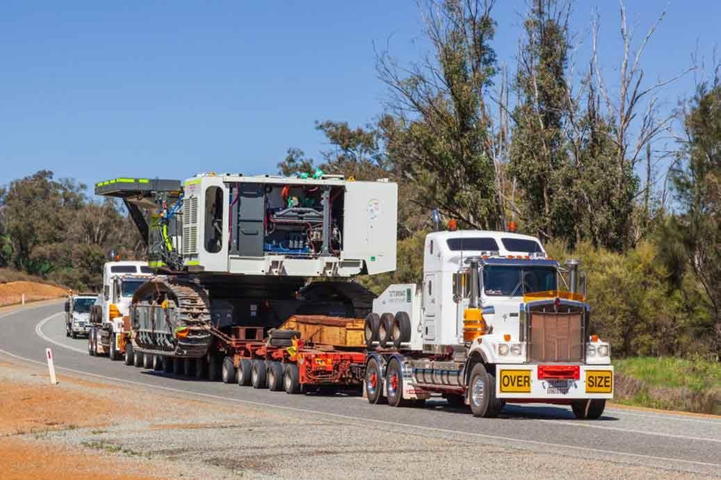 A Semi Truck Is Carrying A Large Machine Down A Road — R2B Heavy Vehicle Driving School In Mackay, QLD