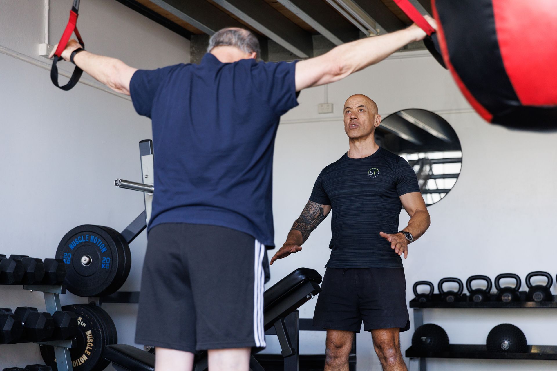 Trainer assists a man using resistance bands in a gym. Black and red medicine ball overhead.