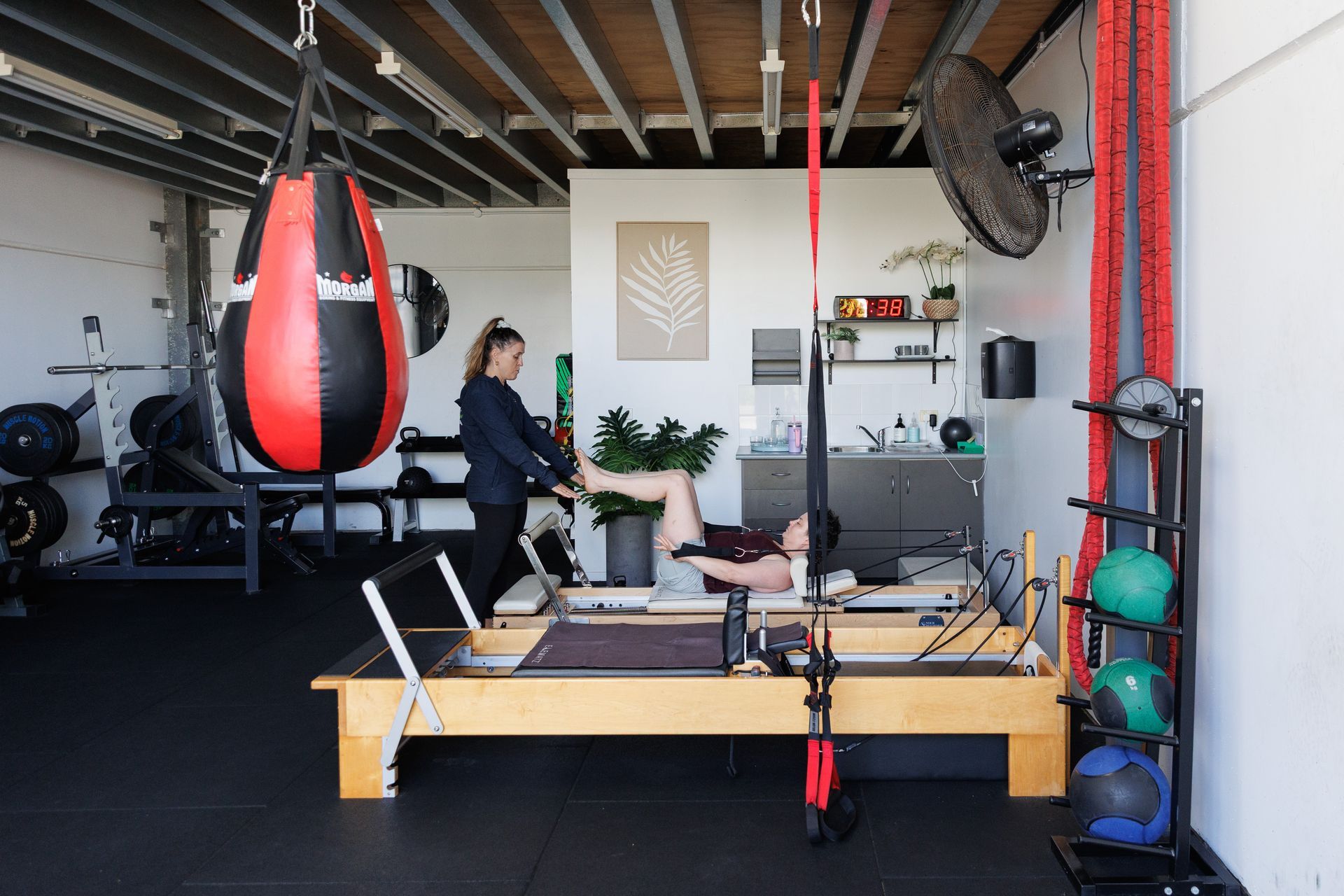Pilates reformer: a person exercises with instructor. Punching bag and weights in the background.