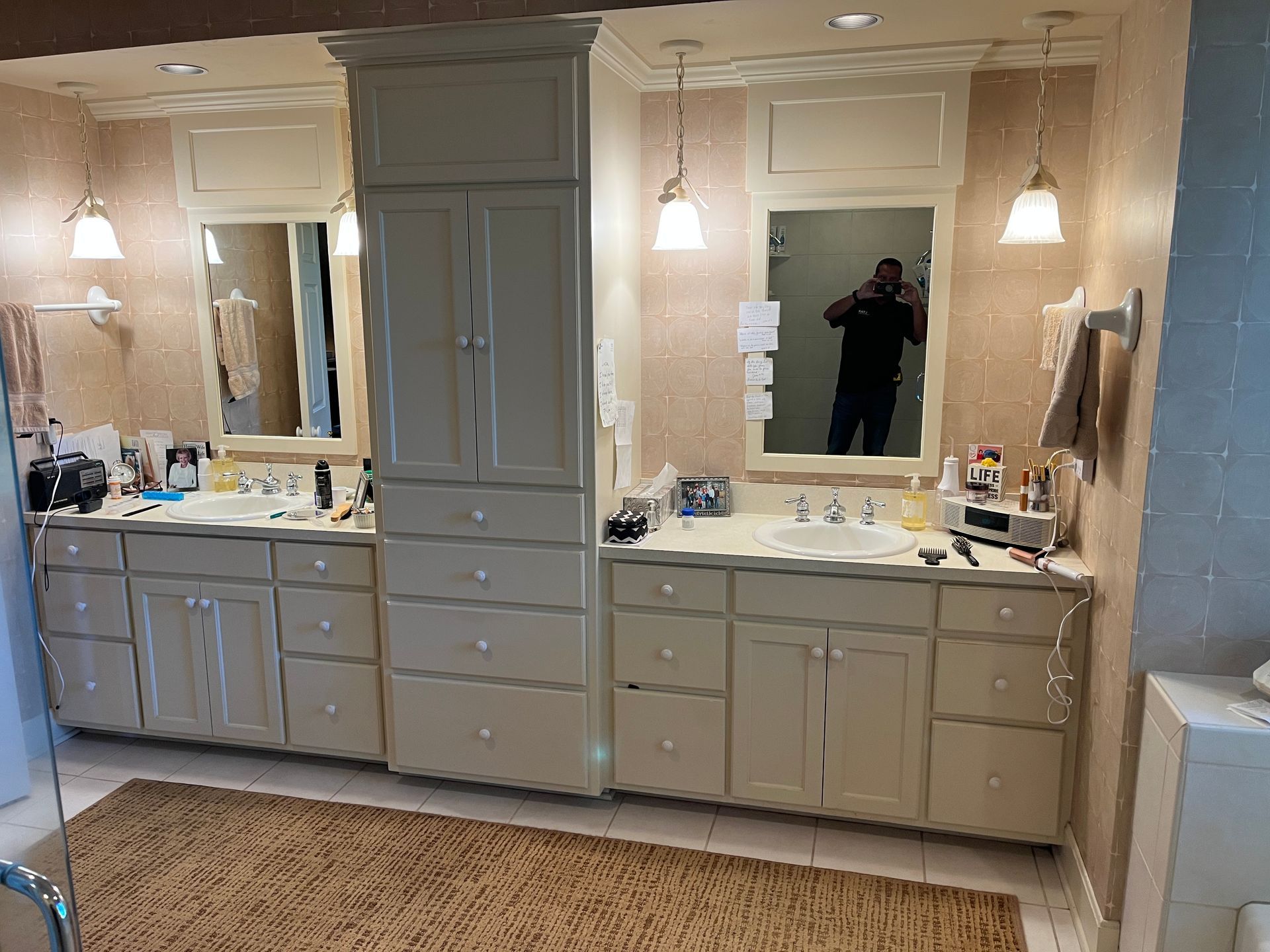 Two white bathroom vanities with mirrors, cream walls, and a brown rug.