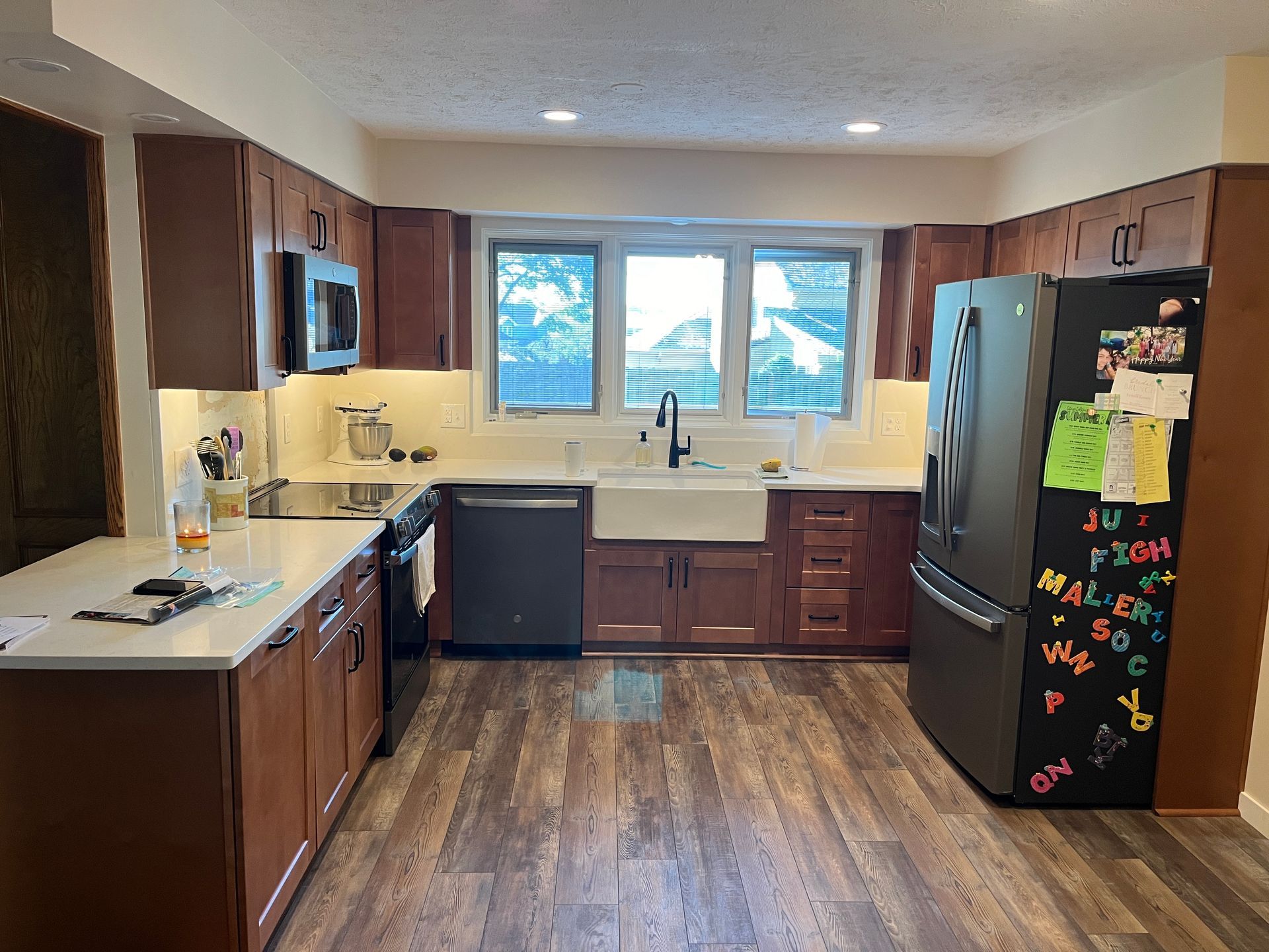 A kitchen with brown cabinets , a black refrigerator and a white sink.