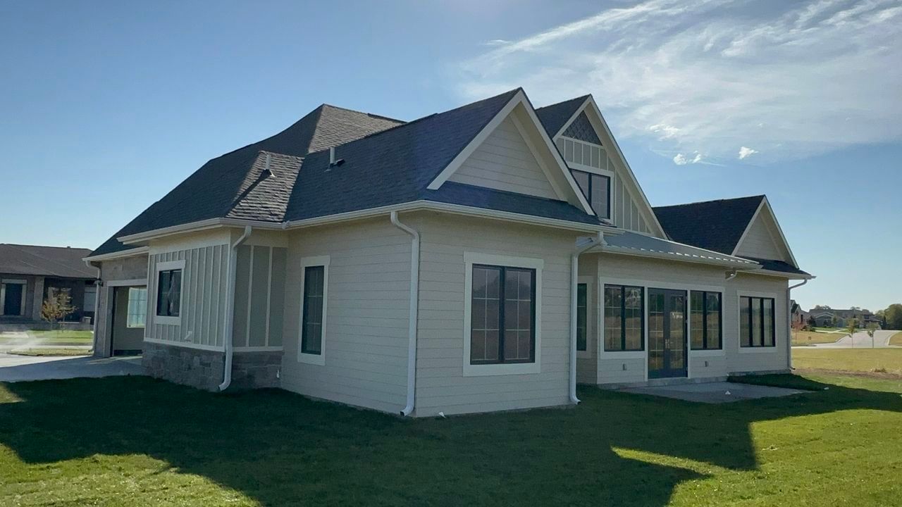 A white house with a black roof is sitting on top of a lush green field.