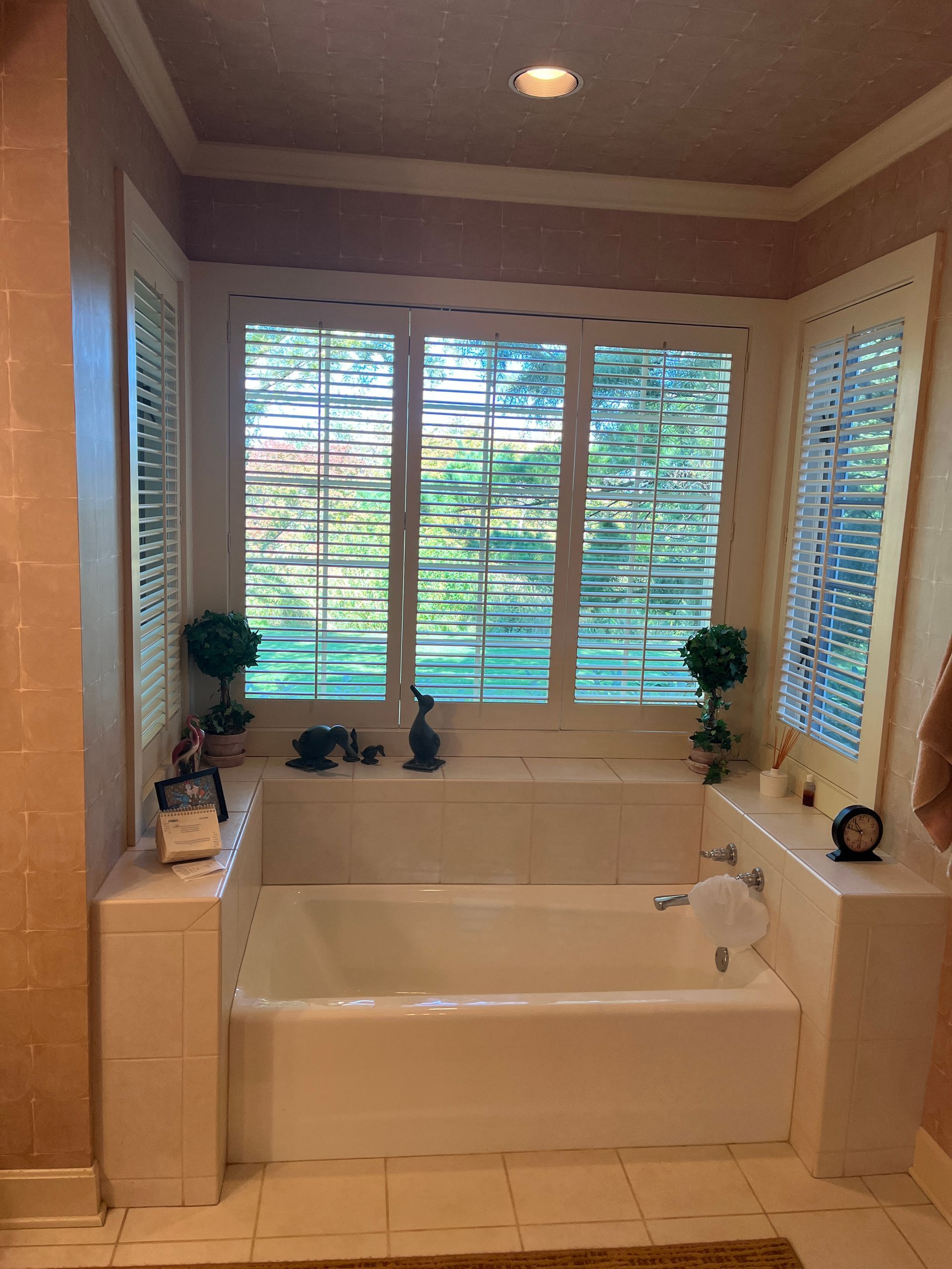 Bathroom with a white tub set beneath a window with blinds and surrounding stone walls.