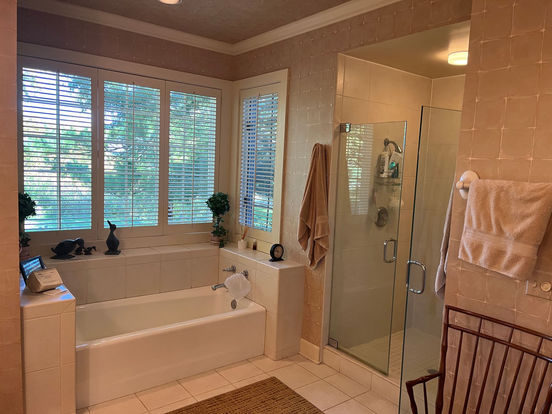 Bathroom with a tub, shower, and window with blinds; light color scheme.