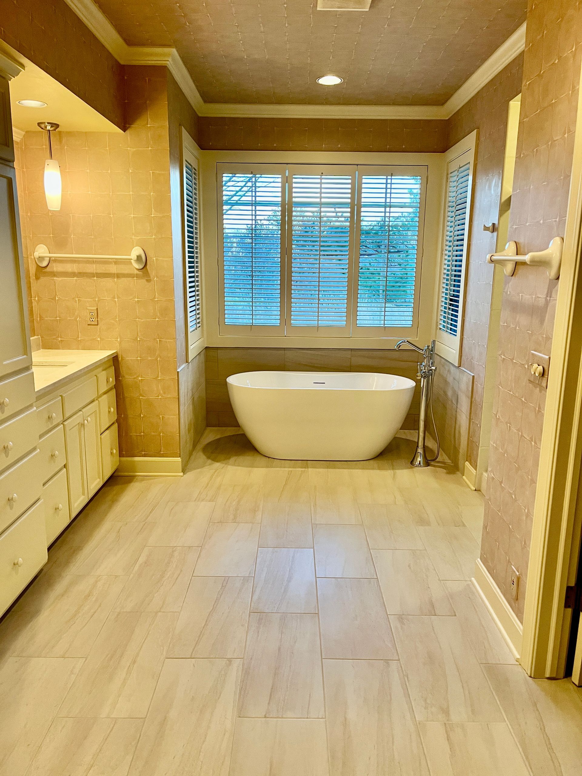 Bathroom with a white freestanding tub in front of a window, light-colored walls, and tile floor.