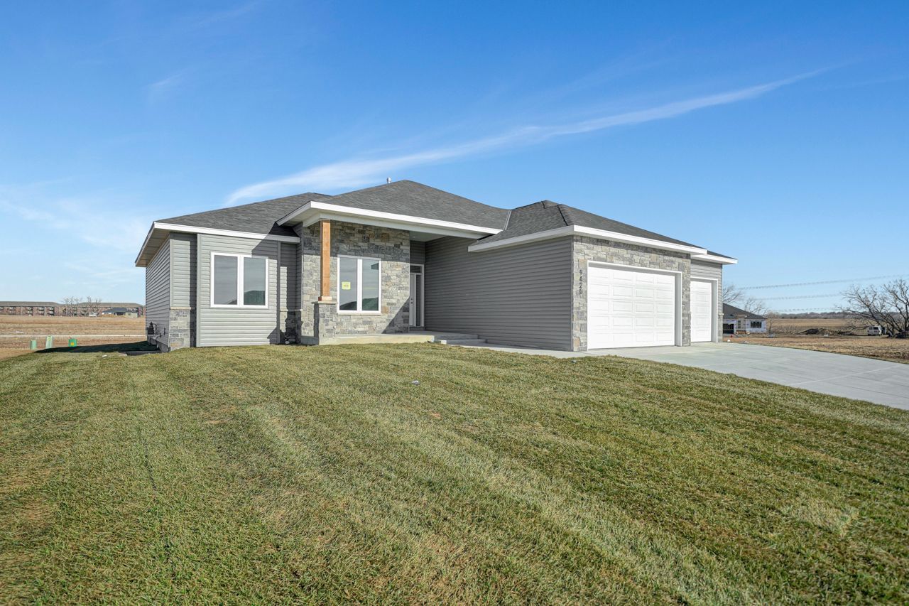 A house with two garages is sitting on top of a lush green field.