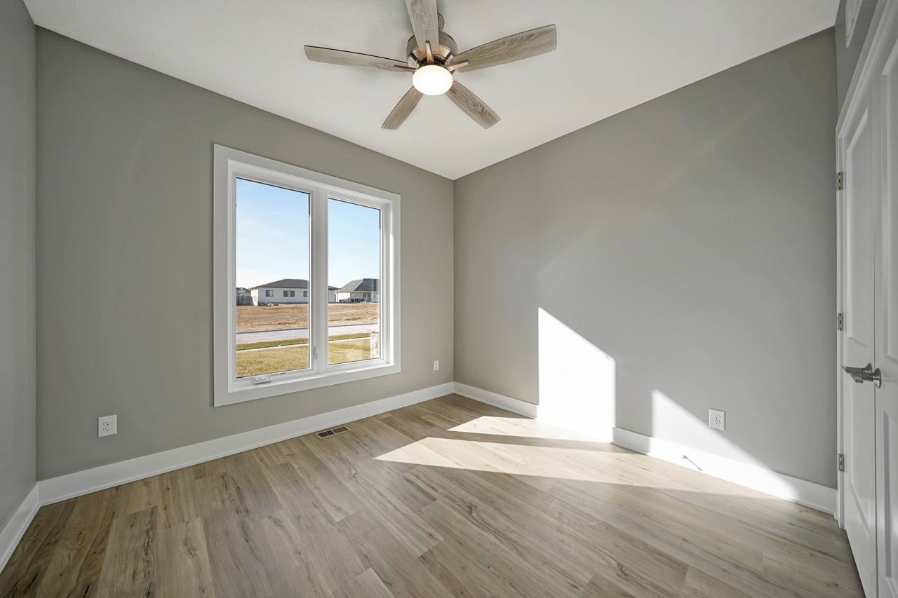 An empty room with a ceiling fan and two windows.