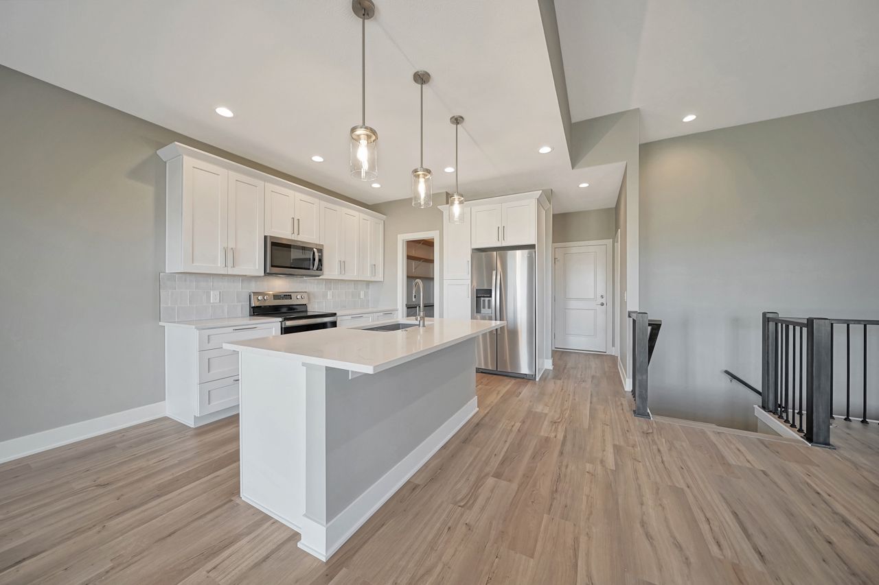 A kitchen with white cabinets , stainless steel appliances , a large island and hardwood floors.