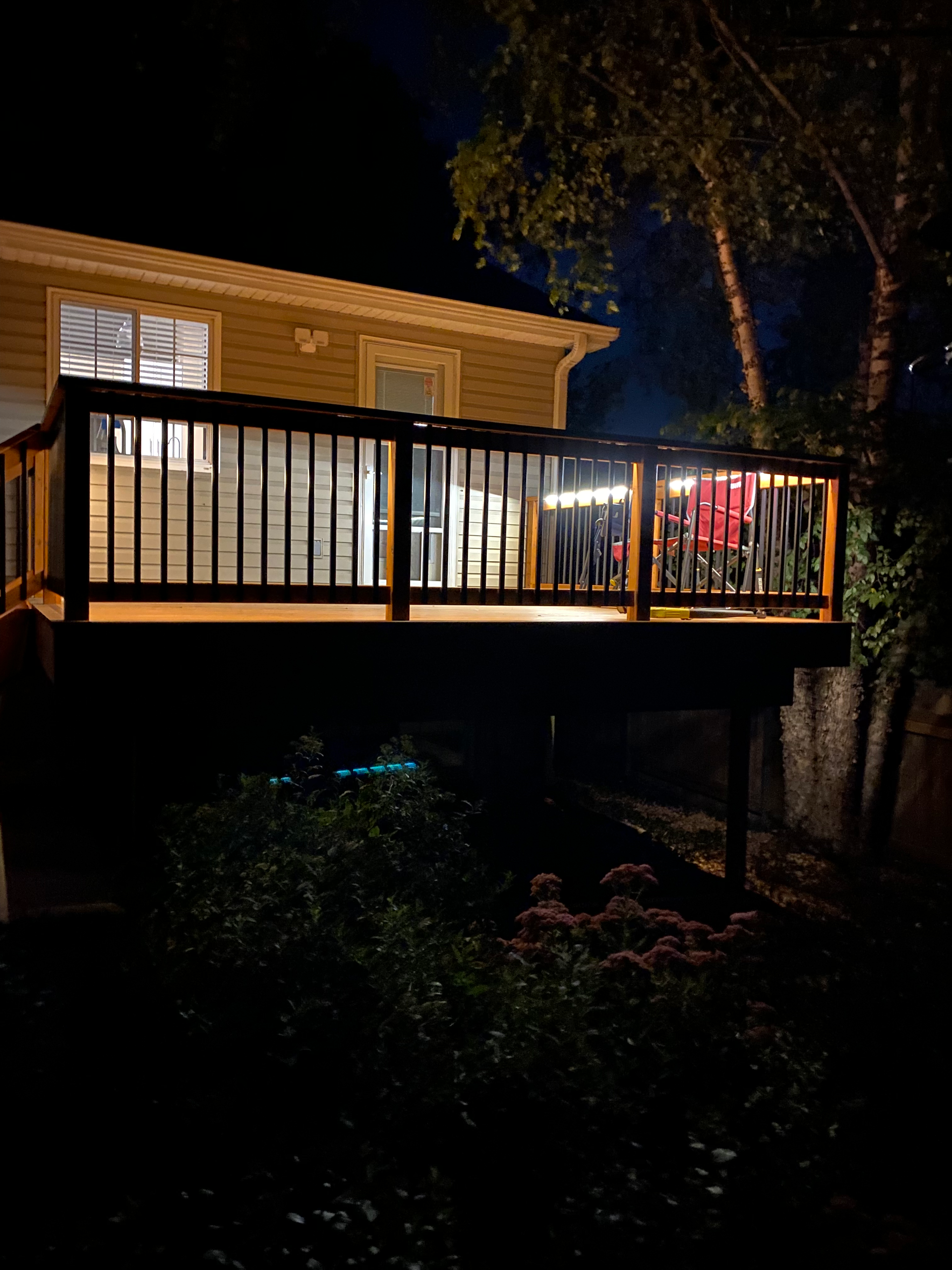 A deck is lit up at night in front of a house.
