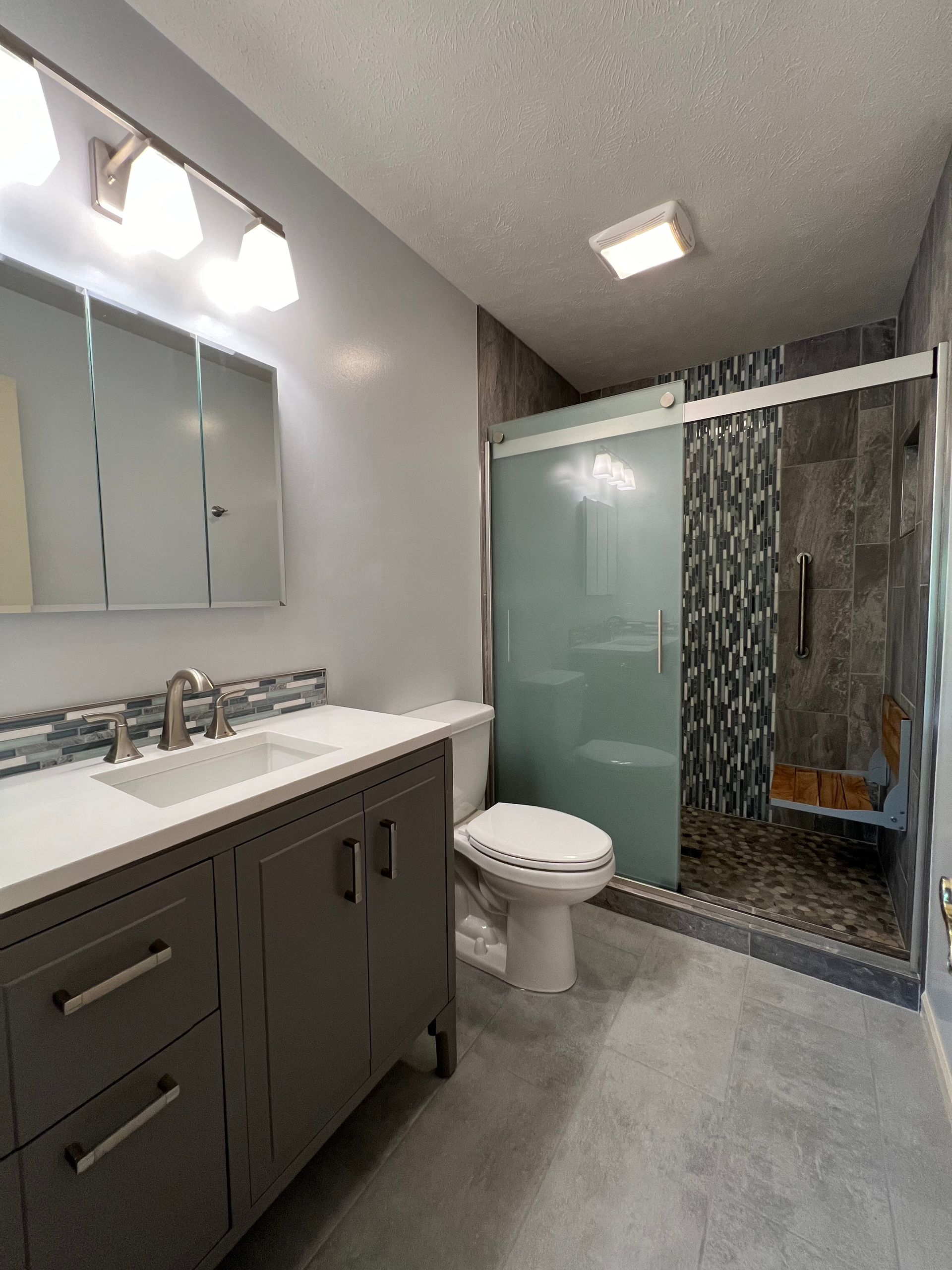 A bathroom with a toilet , sink , mirror and shower.