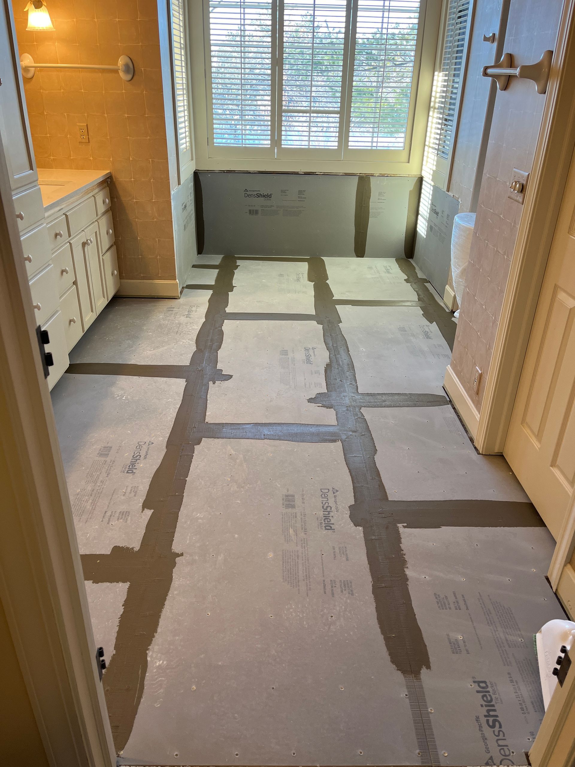 Bathroom floor with gray moisture barrier. Gray grout lines form a grid. Walls are partially covered.