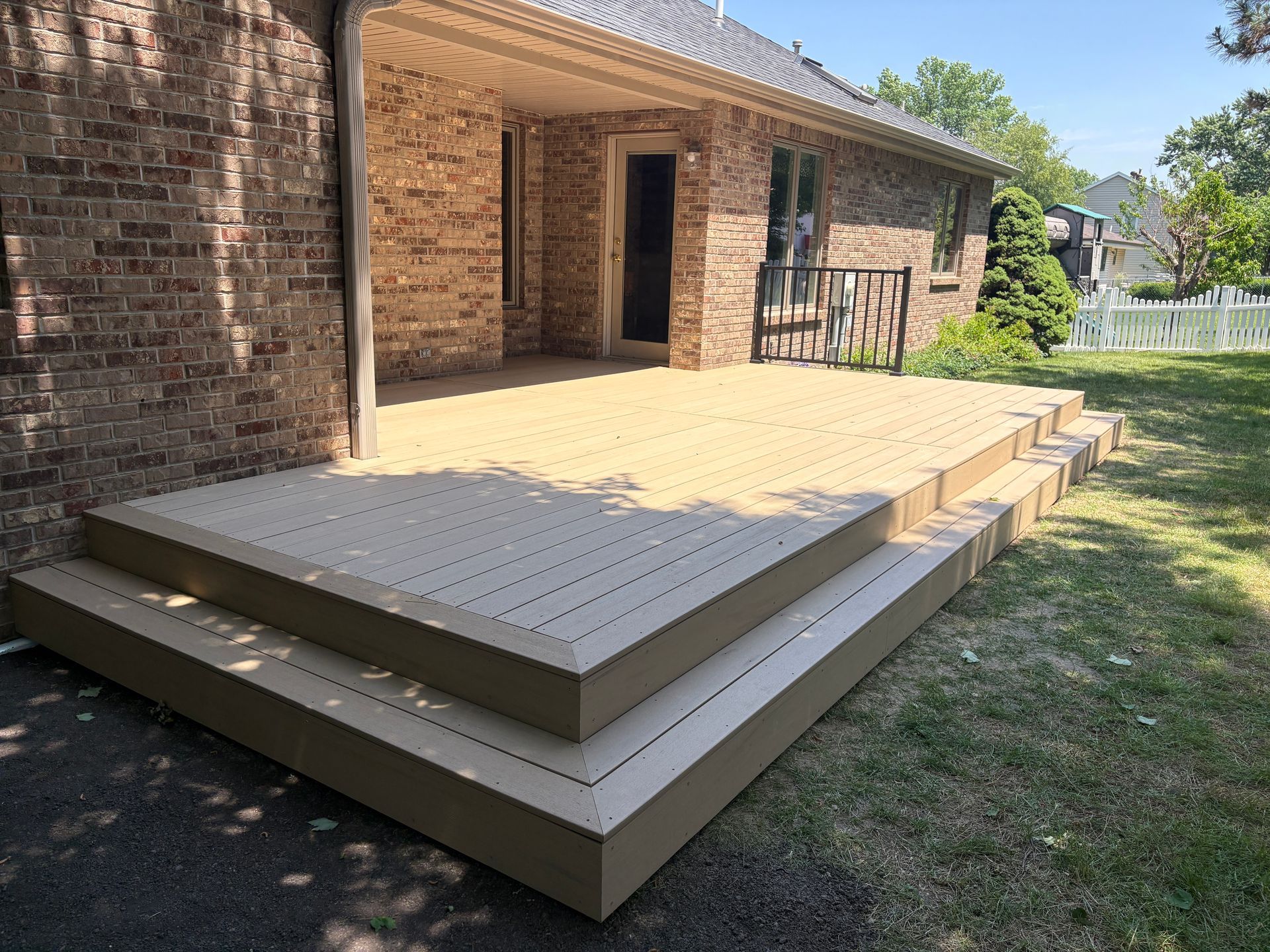Composite deck with two steps, attached to a brick house, on a grassy yard.