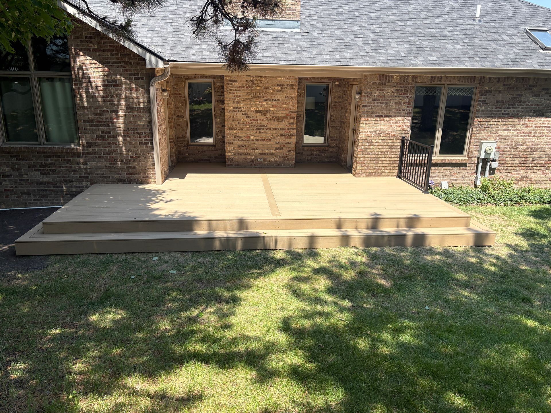 A brick house with a composite deck. Steps lead down to the grassy yard.