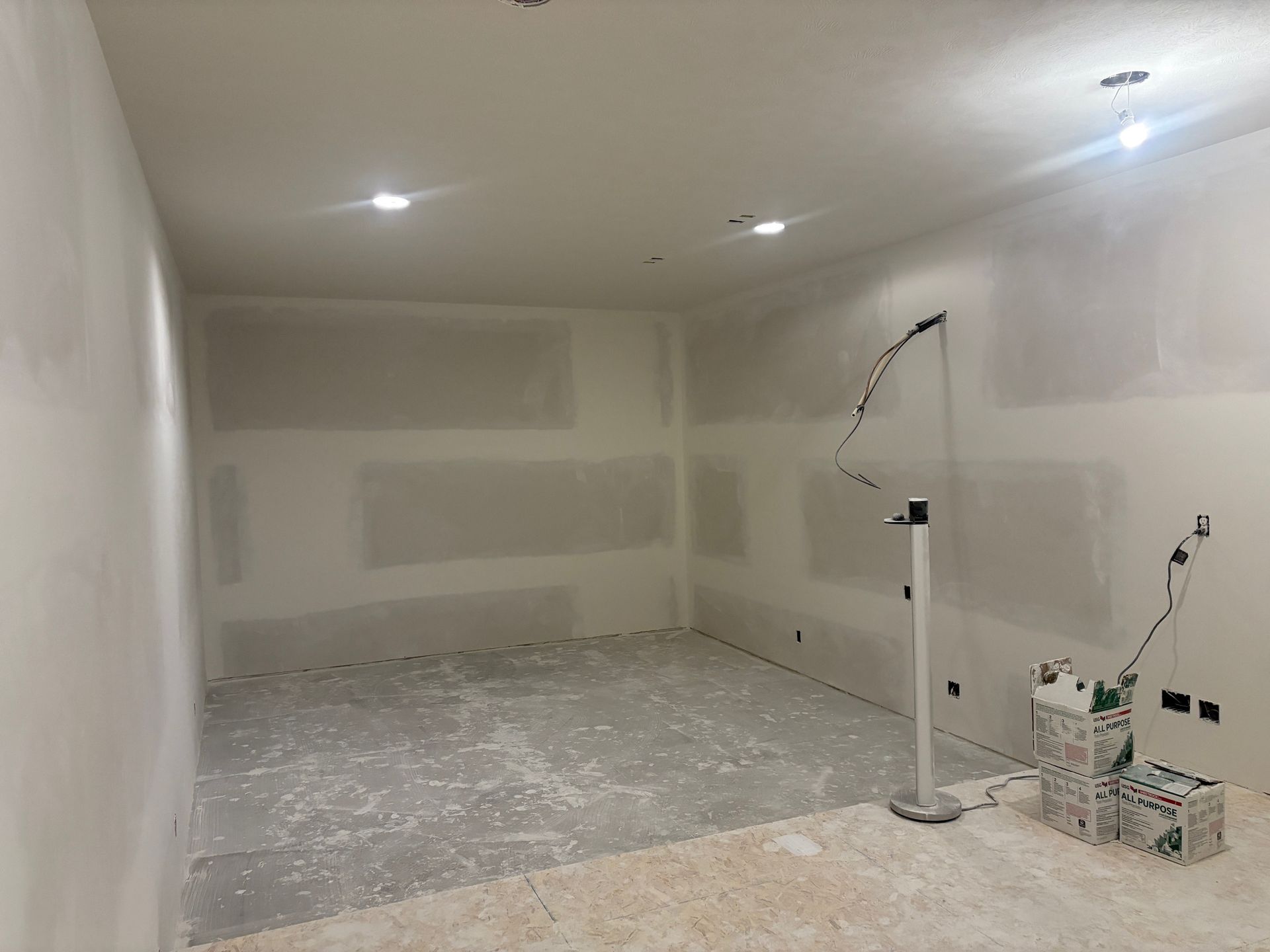 A room with drywall on the walls and a lamp on the floor.