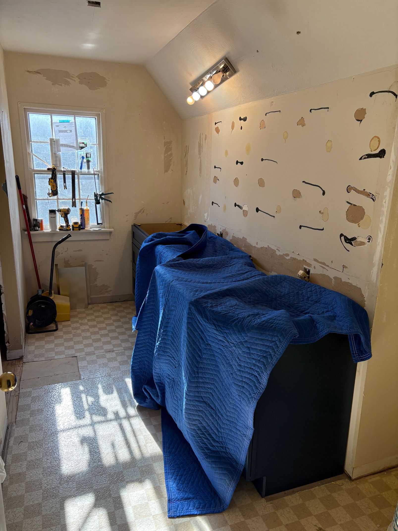 Room undergoing renovation with peeling walls, a window, and blue covered appliance.