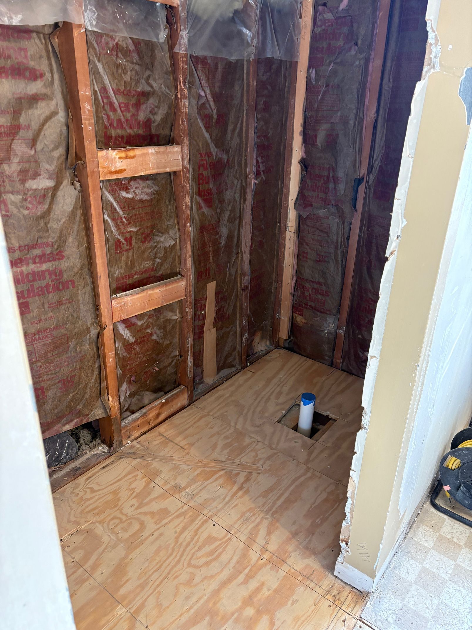 Bathroom renovation in progress, exposed studs and insulation, plywood floor.